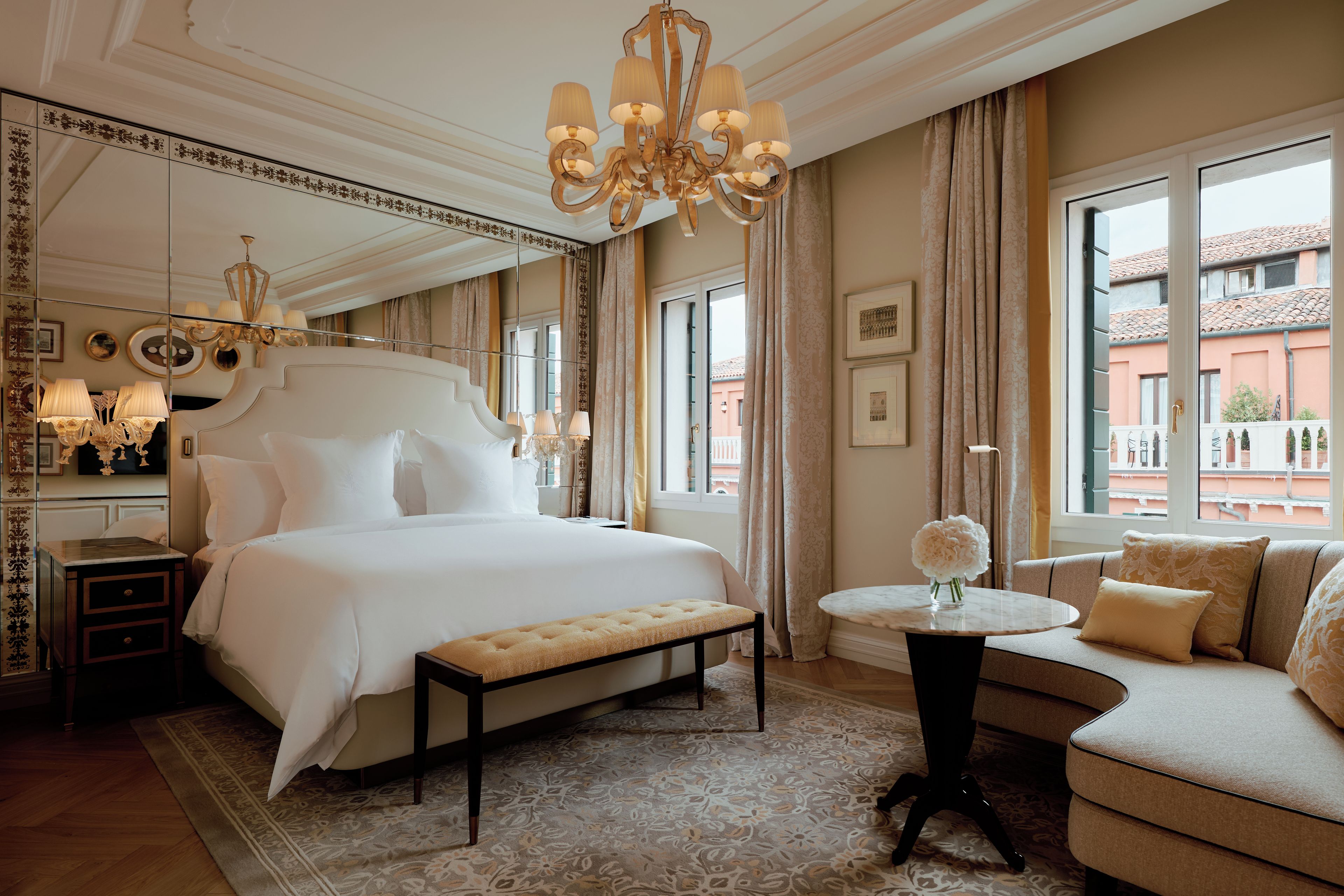 Een hotelkamer met een groot bed, een zithoek met een bank, een klein rond tafeltje en uitzicht op het omliggende landschap.