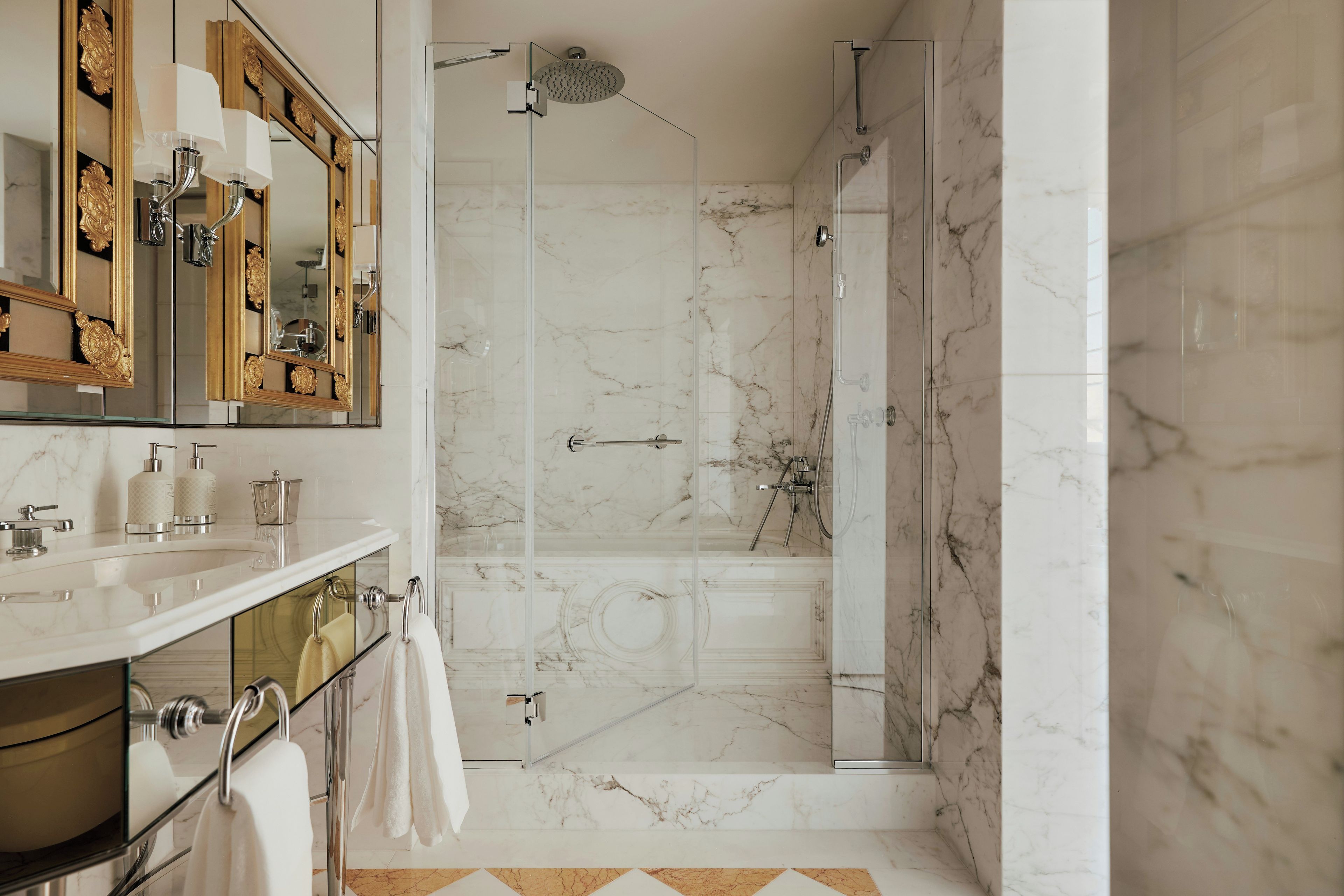 Un bagno con pavimento in marmo, box doccia in vetro e un mobile vanitario con specchio e porta asciugamani.
