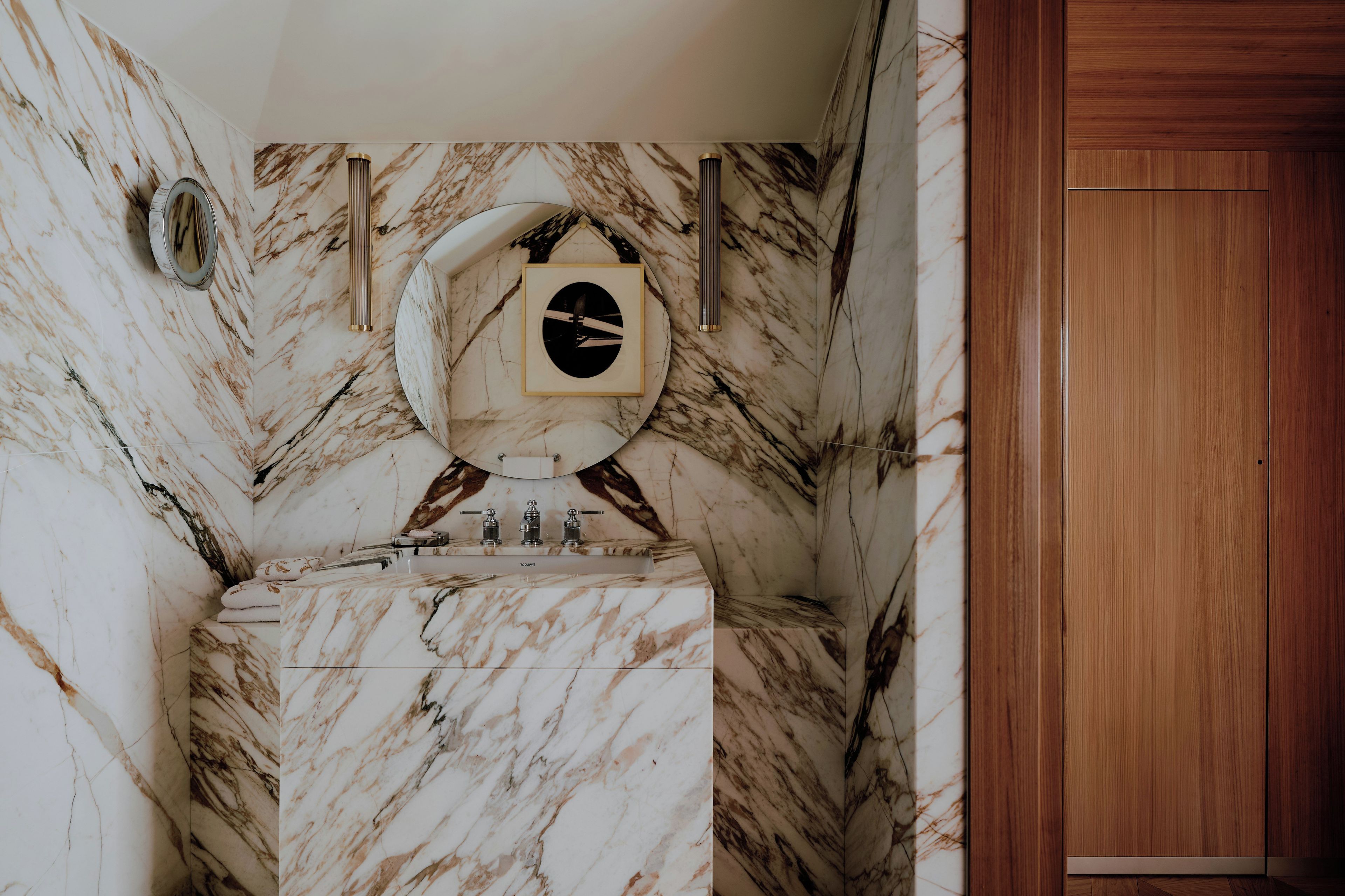 A bathroom with a marble sink, a mirror, and a wooden door.