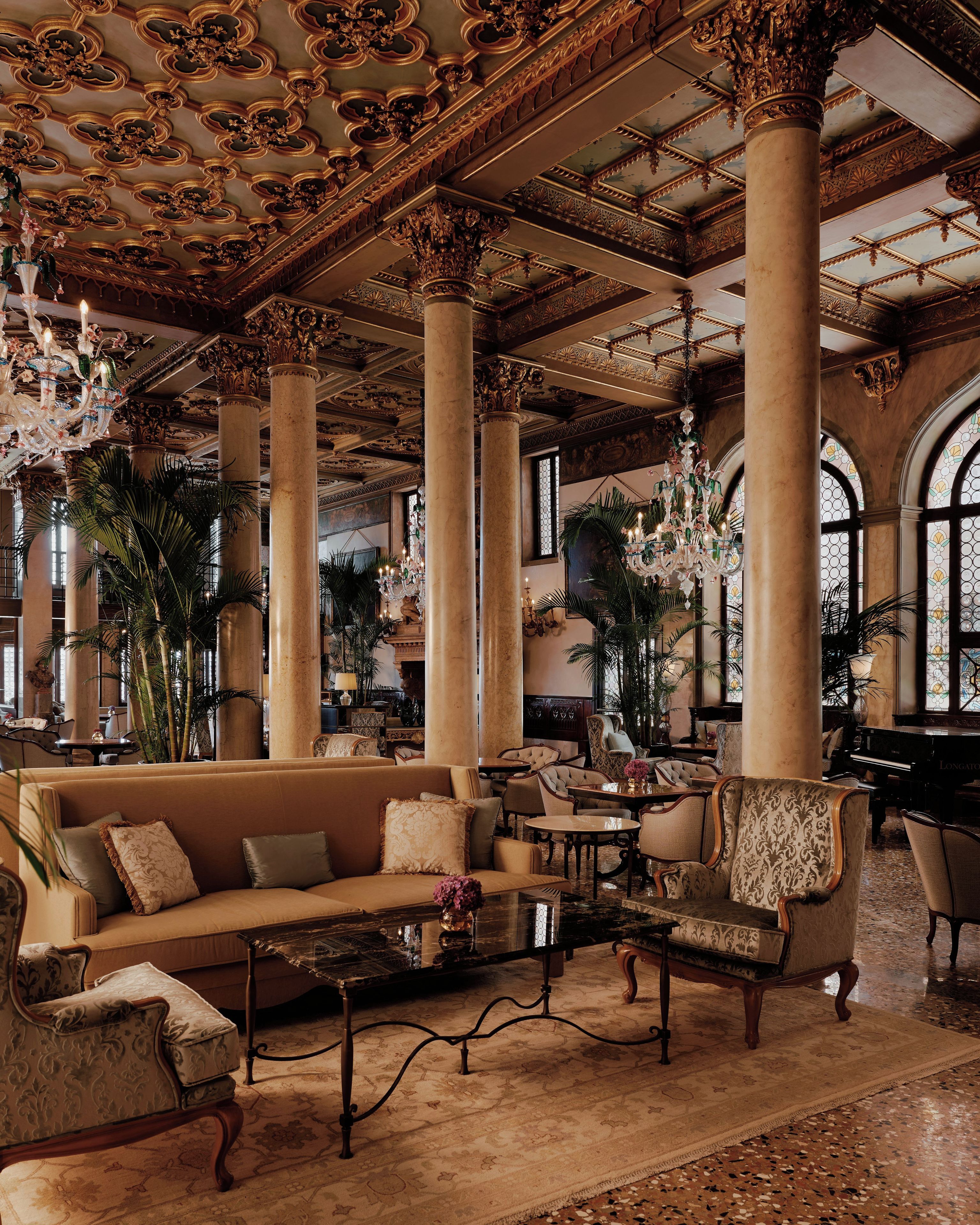 A grand lobby with ornate columns, chandeliers, and a piano.