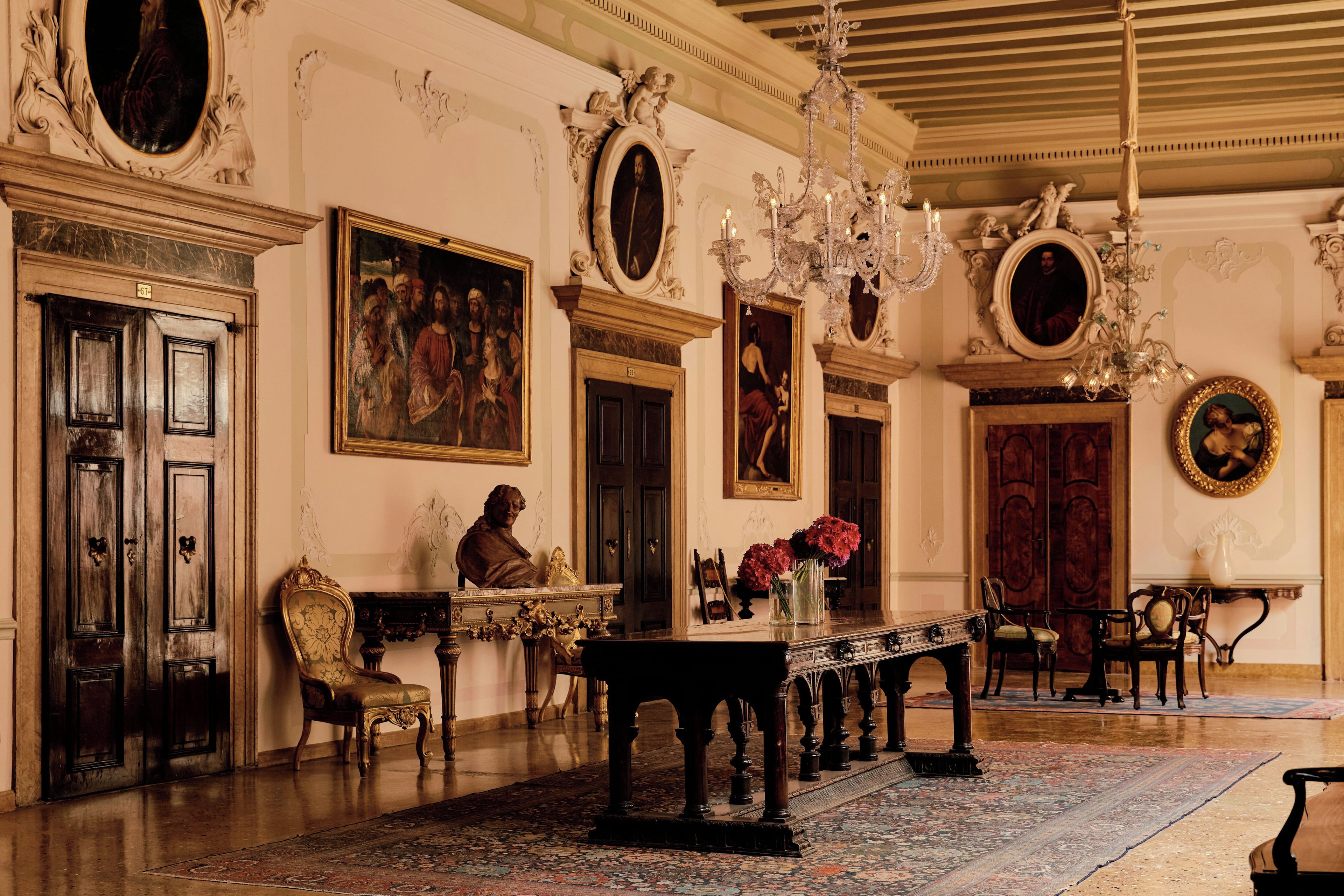Um salão imponente com decoração requintada, uma mesa comprida e pinturas clássicas.
