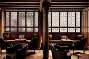 A room with wooden paneled walls, a large stained glass window, and a bench with chairs.