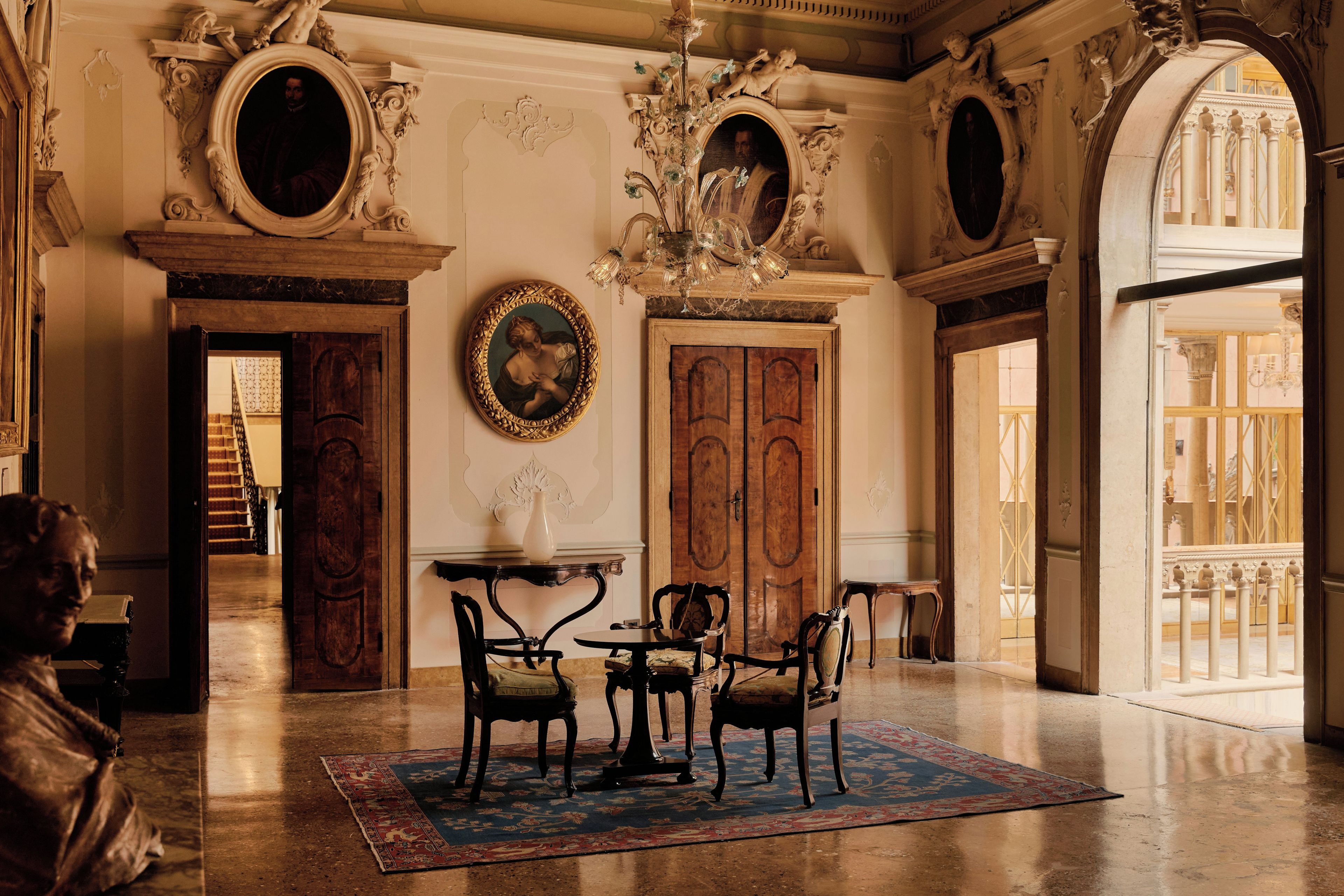 Una stanza decorata con architettura classica, che include una maestosa scalinata, un lampadario e un'ampia porta in legno.