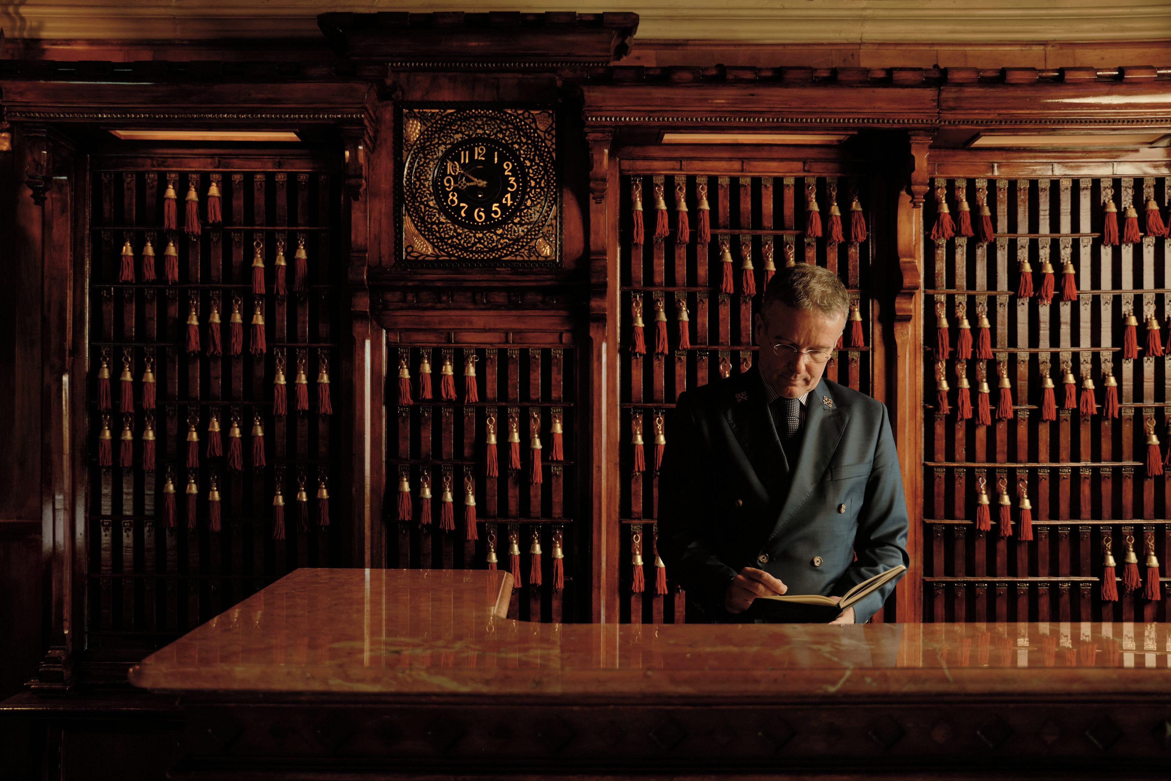 Un uomo legge un libro in una stanza con pareti in legno e un grande orologio.