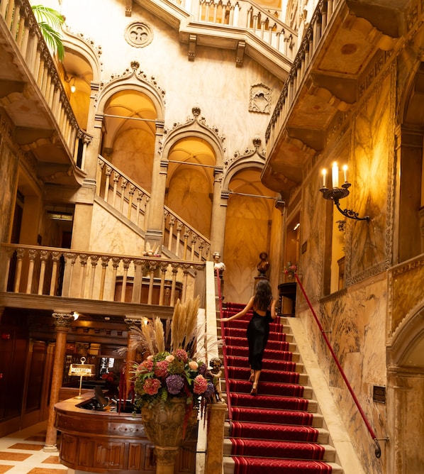 Un'imponente scalinata con tappeto rosso, ringhiere decorate e una reception con un'elegante composizione floreale.