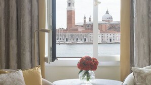 A room with two armchairs, a small table with a vase of flowers, and a view of a historic building across the water. - Danieli, Venezia, A Four Seasons Hotel (Venice)