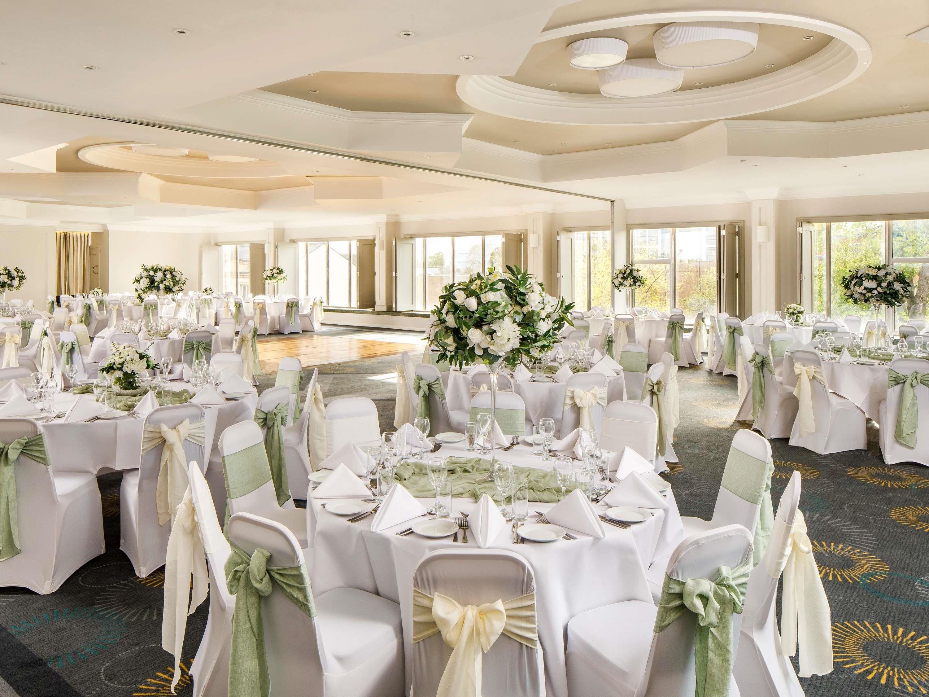 A banquet hall with round tables, chairs, and floral centerpieces.