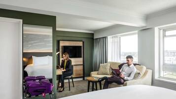 Quarto de hotel com cama, escrivaninha, sofá e vista para a cidade.