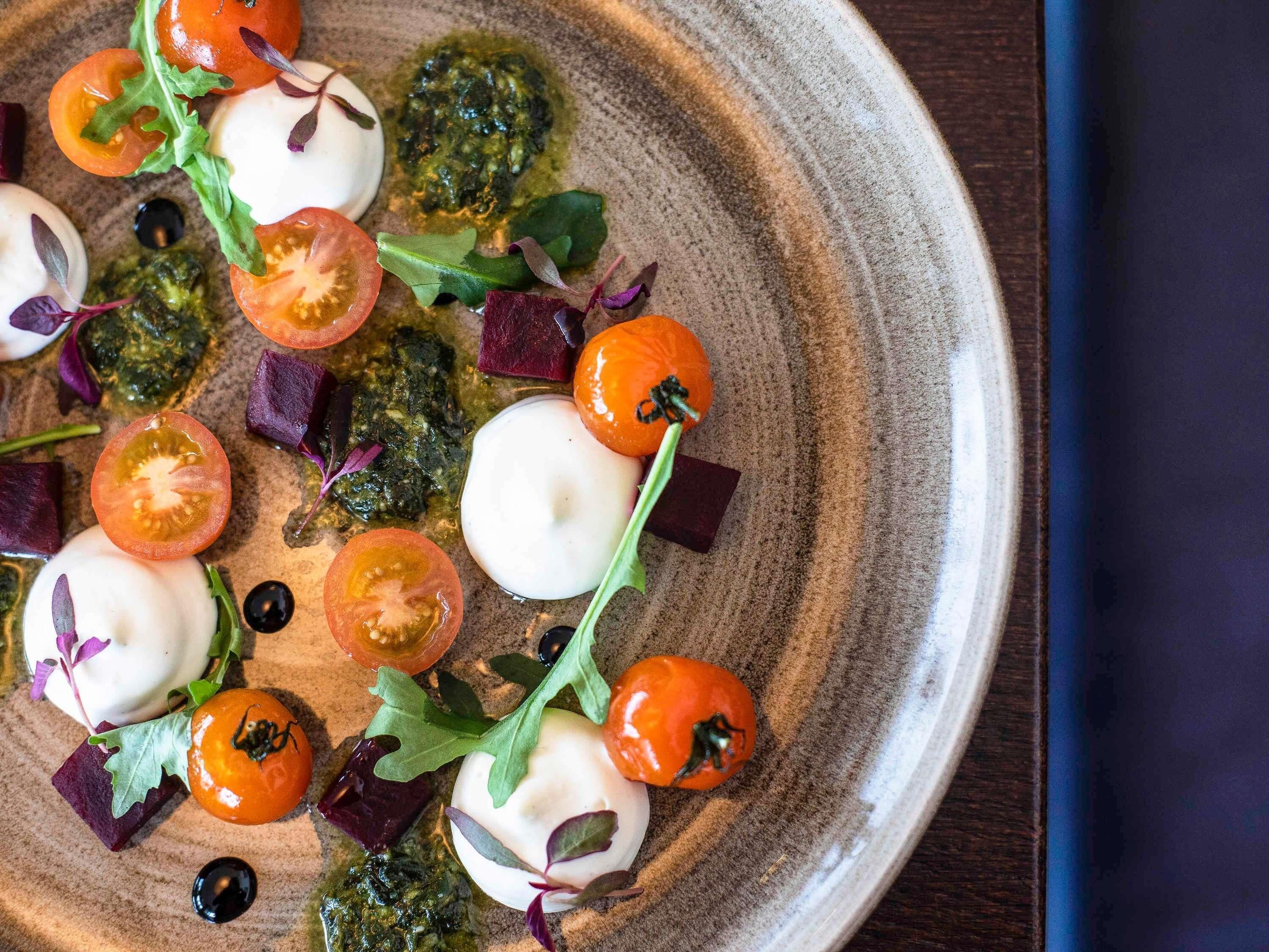 A plate with a variety of food items including tomatoes, greens, and a dollop of cream.