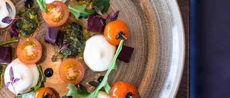 A plate with a variety of food items including tomatoes, greens, and a dollop of cream.