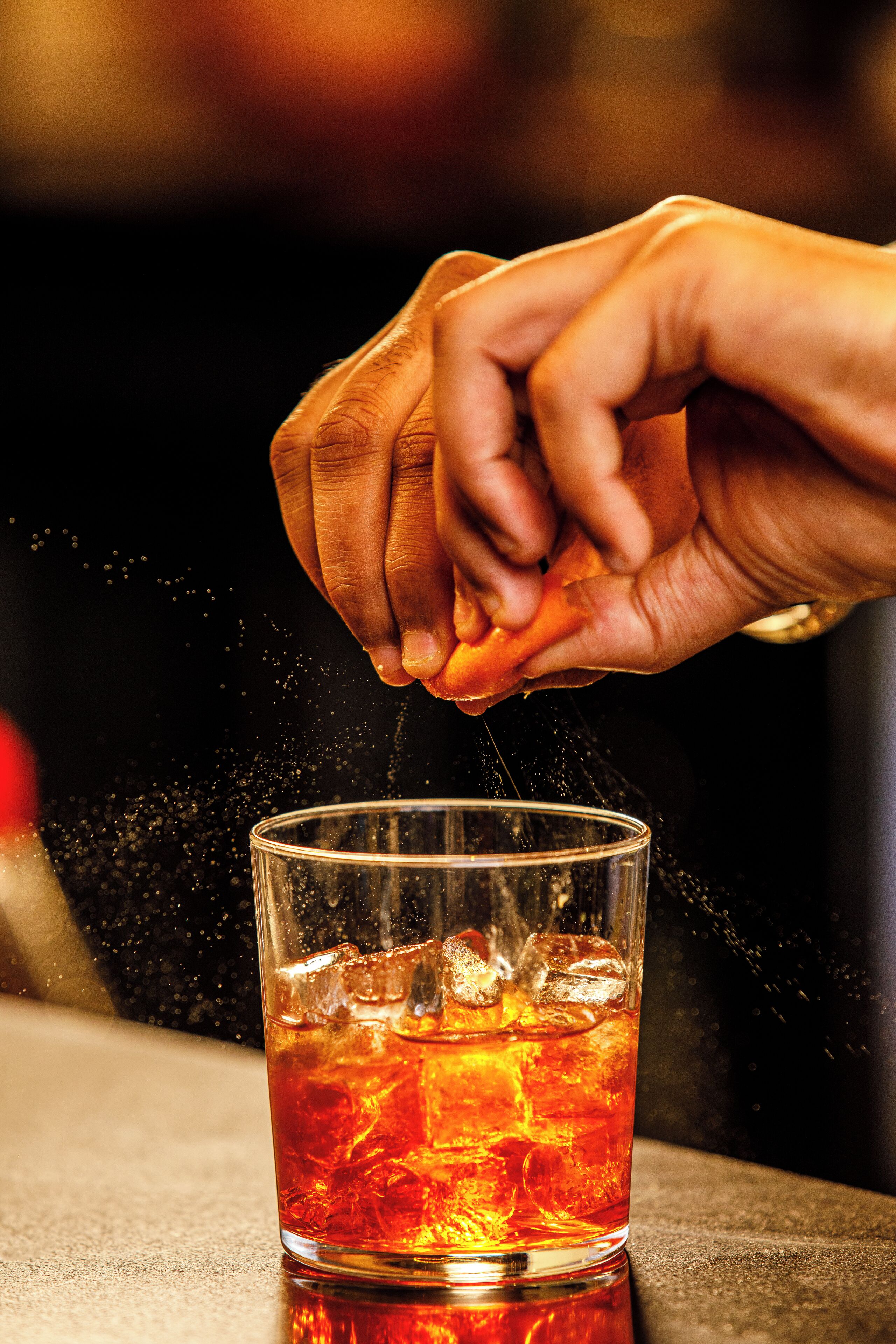 A hand squeezing a citrus fruit over a glass with ice cubes.