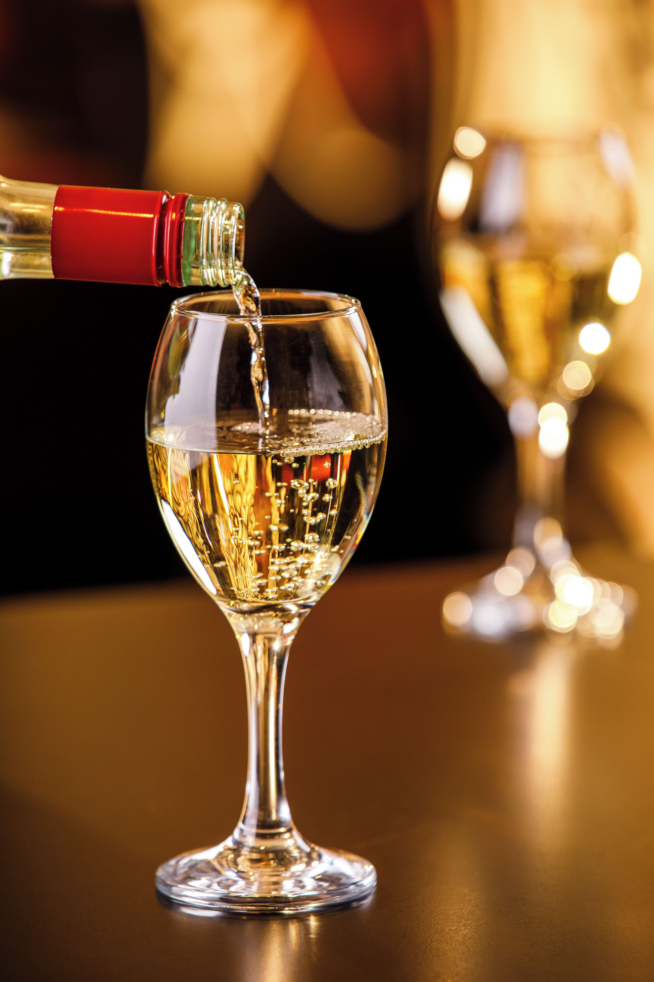 Una copa de vino siendo servida con un líquido transparente, presumiblemente vino, con una botella en primer plano.