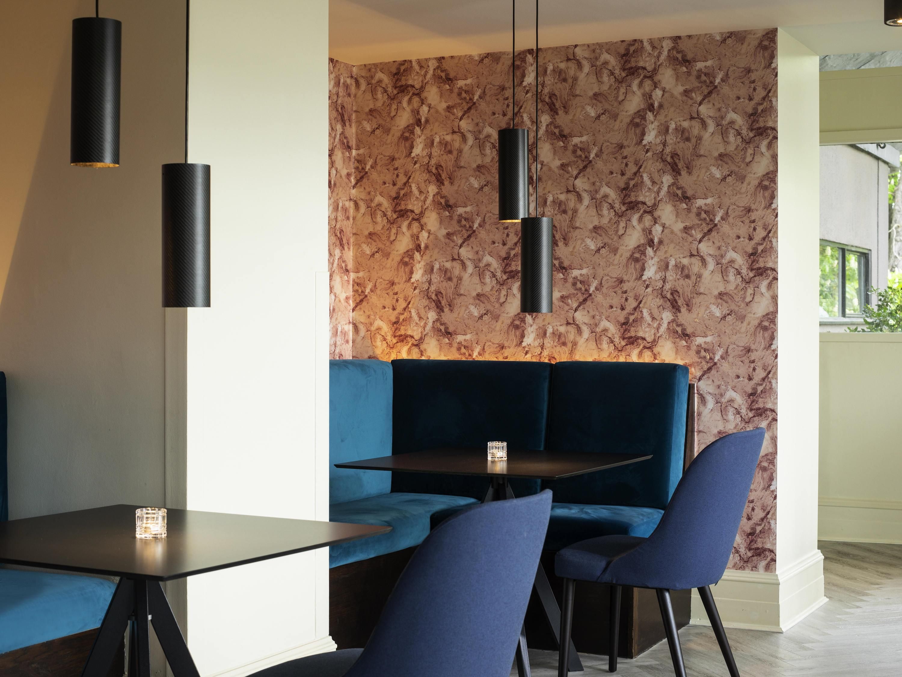 A modern dining area with a dark table, blue seating, and pendant lights.
