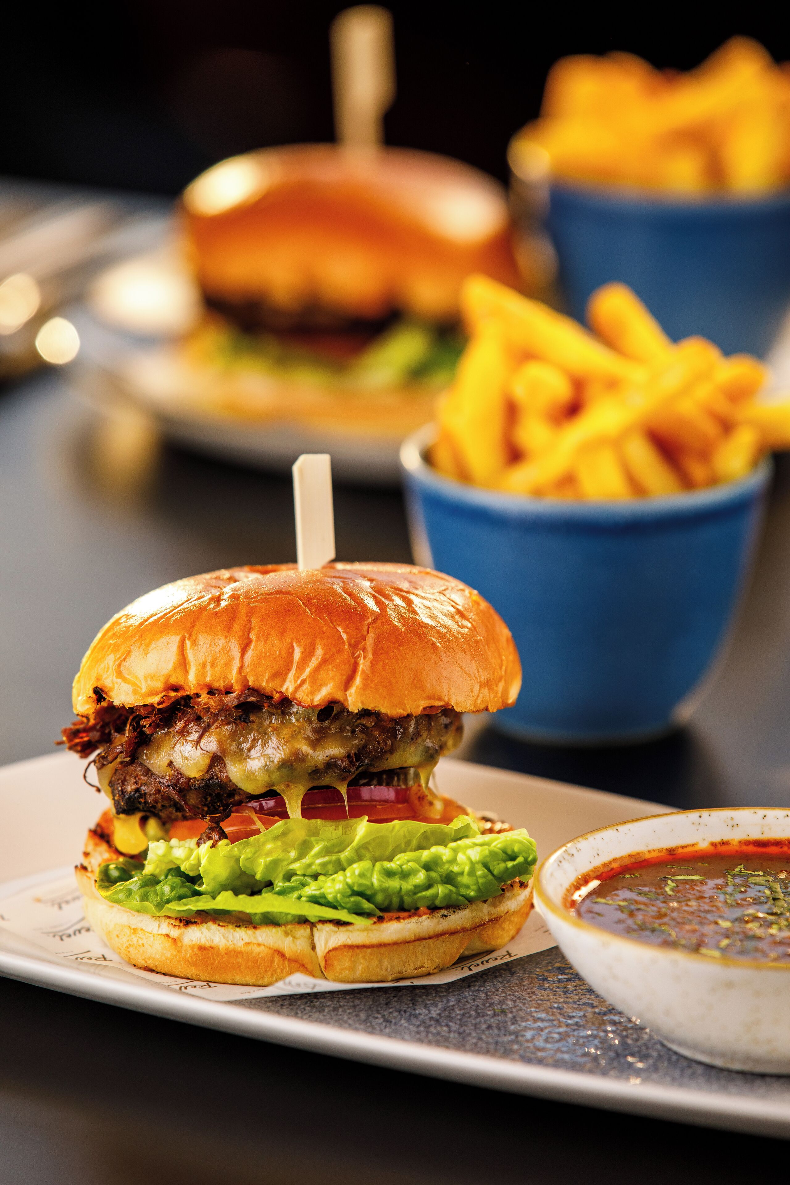 A burger with fries and a side of sauce on a plate.