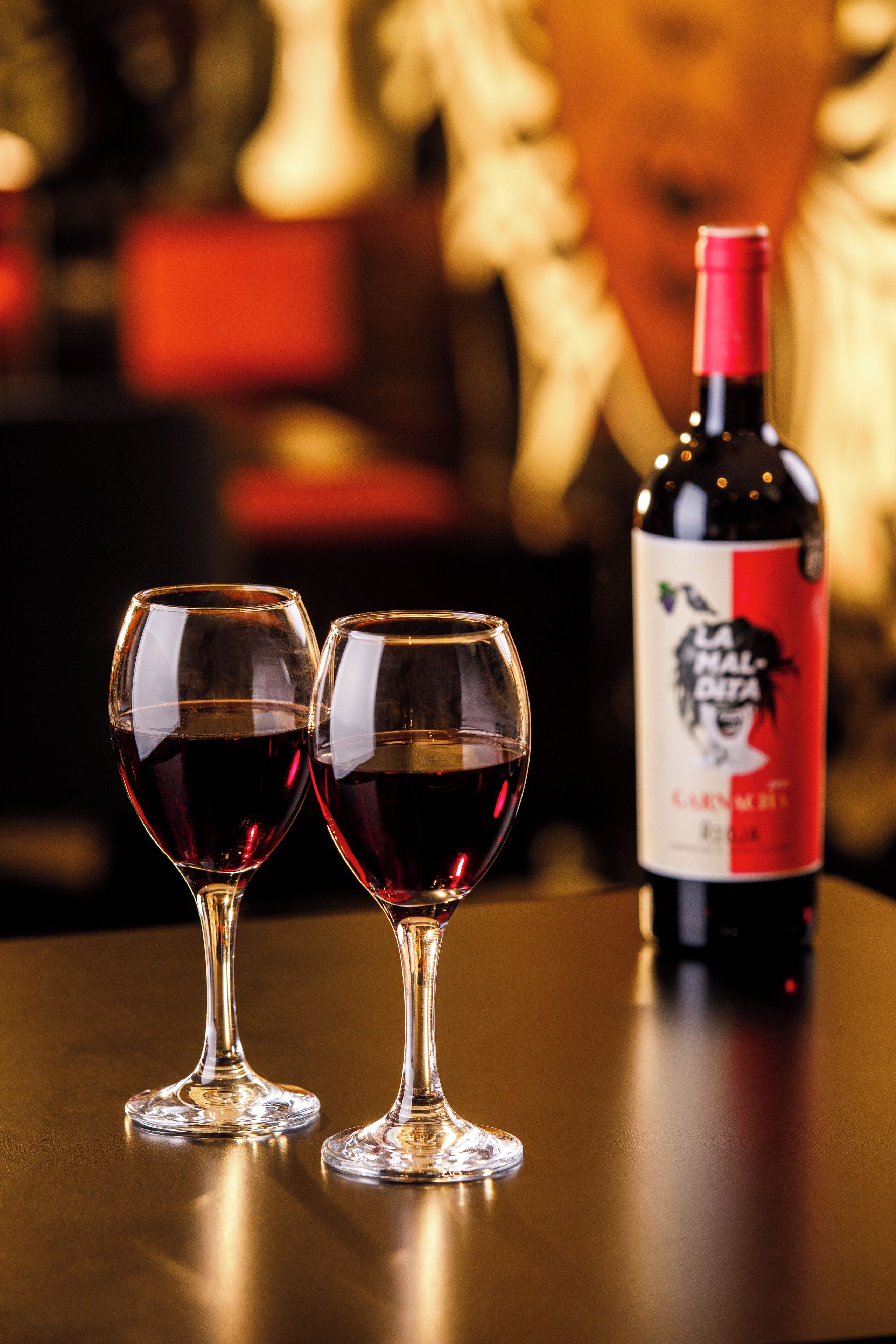 Two wine glasses on a table with a bottle of wine in the background.