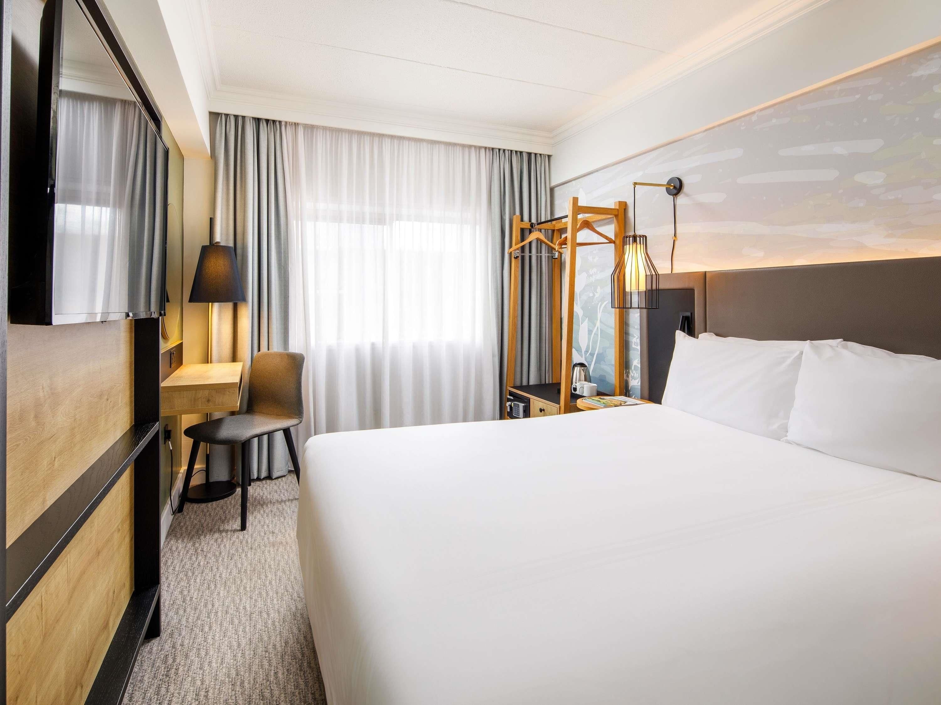 A hotel room with a large bed, a desk with a chair, a TV, and a window with curtains.