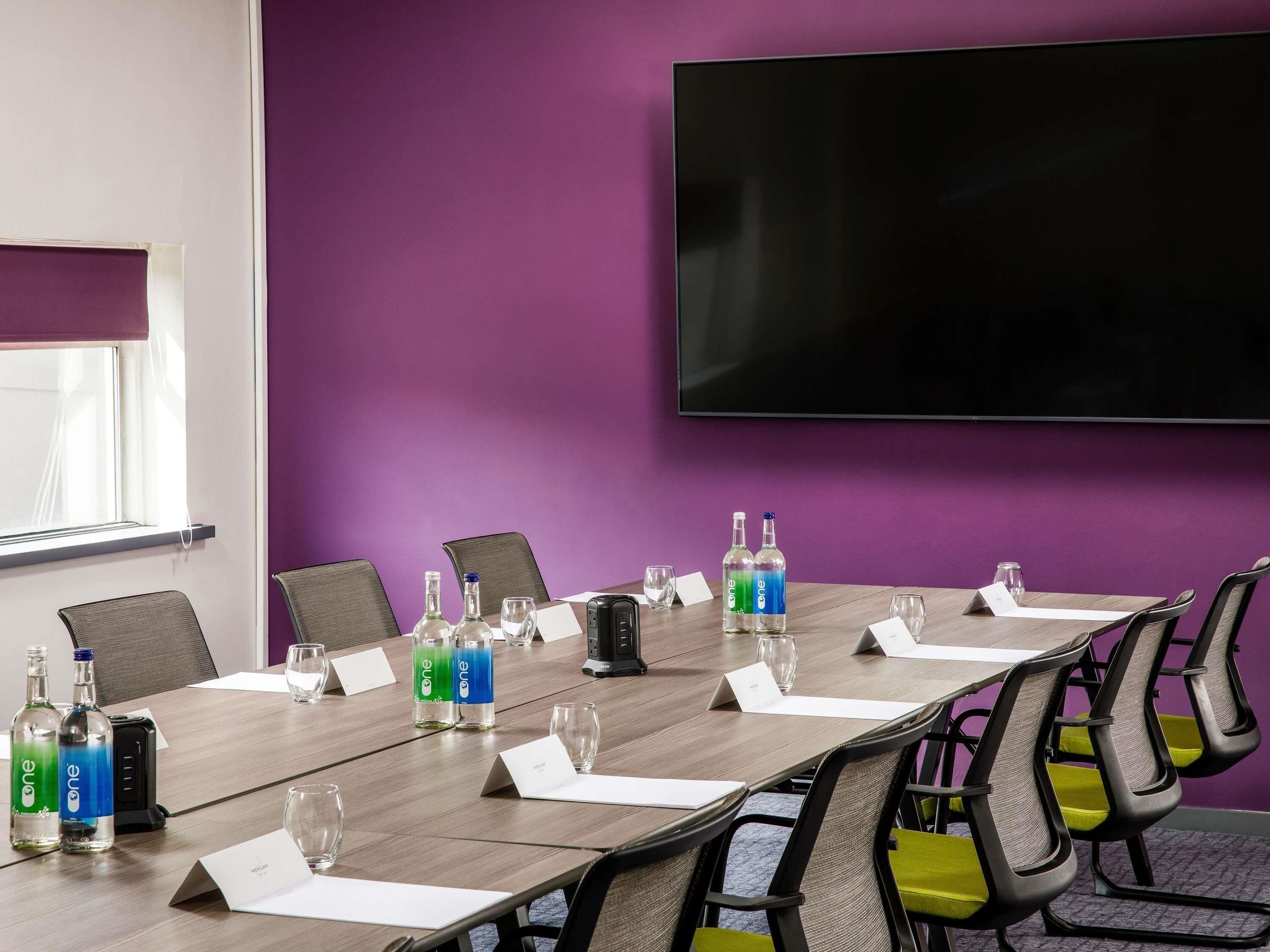 A conference room with a long table, chairs, a TV screen, and name cards.