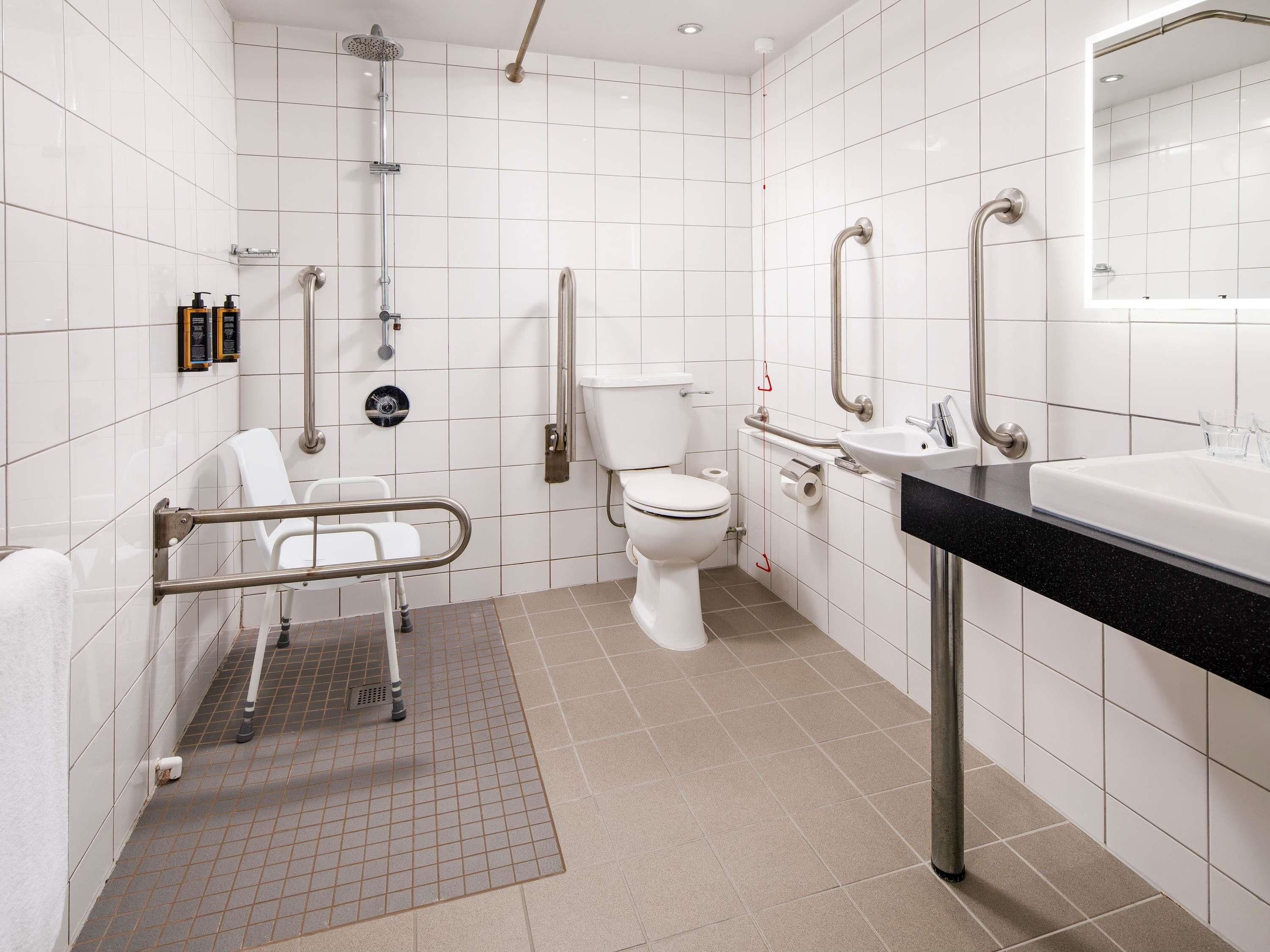 Un bagno moderno dotato di doccia, WC e lavandino, provvisto di maniglie di sostegno e una sedia a rotelle per la doccia.