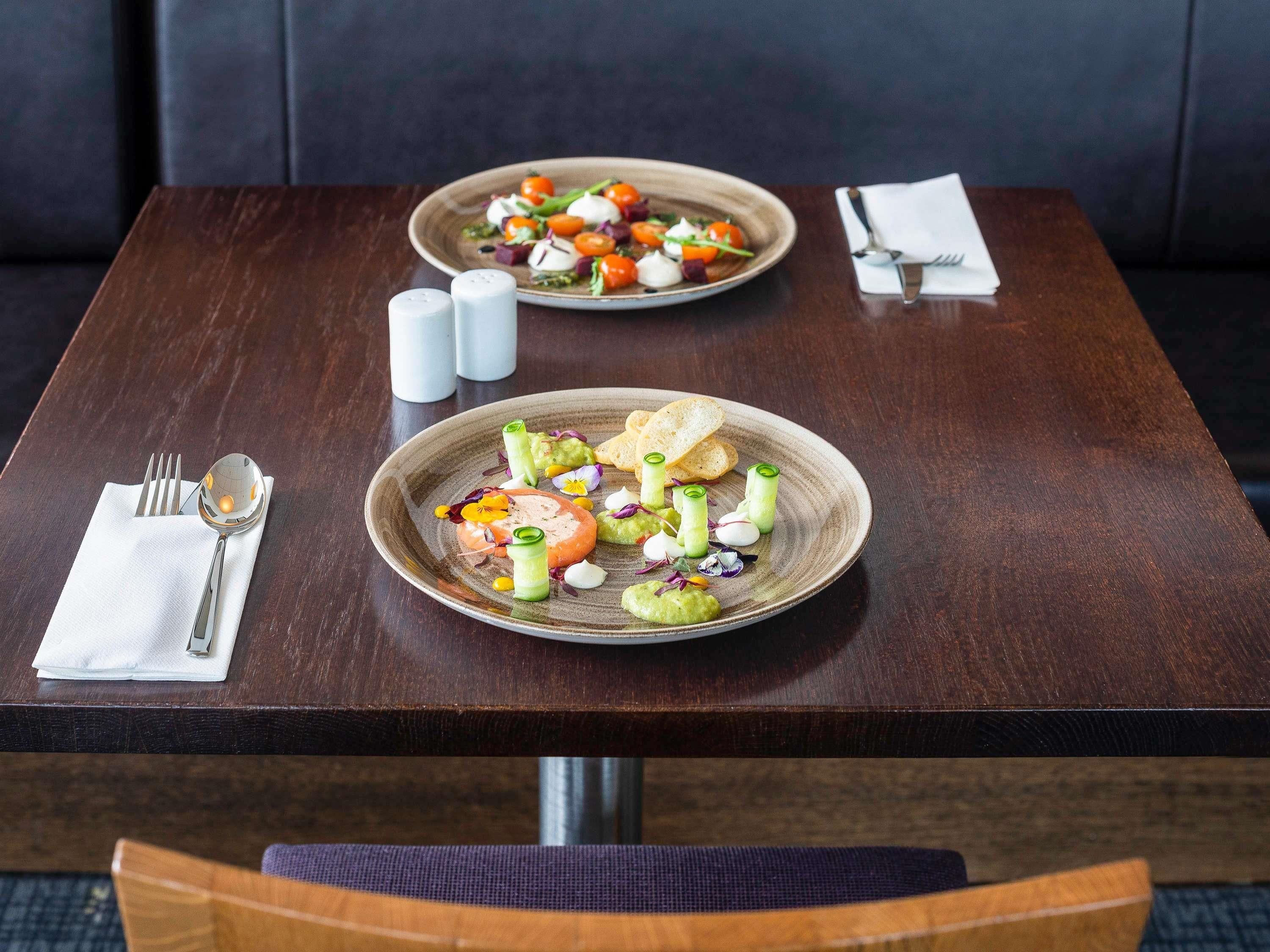 A dining table with plates of food, cutlery, and salt and pepper shakers.