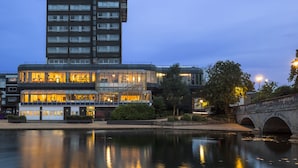 Ein modernes Hotel mit mehreren Etagen, einer Glasfassade und Spiegelung im Wasser.