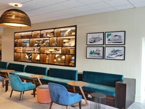 Un espace de détente moderne avec des canapés turquoise, une bibliothèque en bois et des œuvres d’art maritimes encadrées.