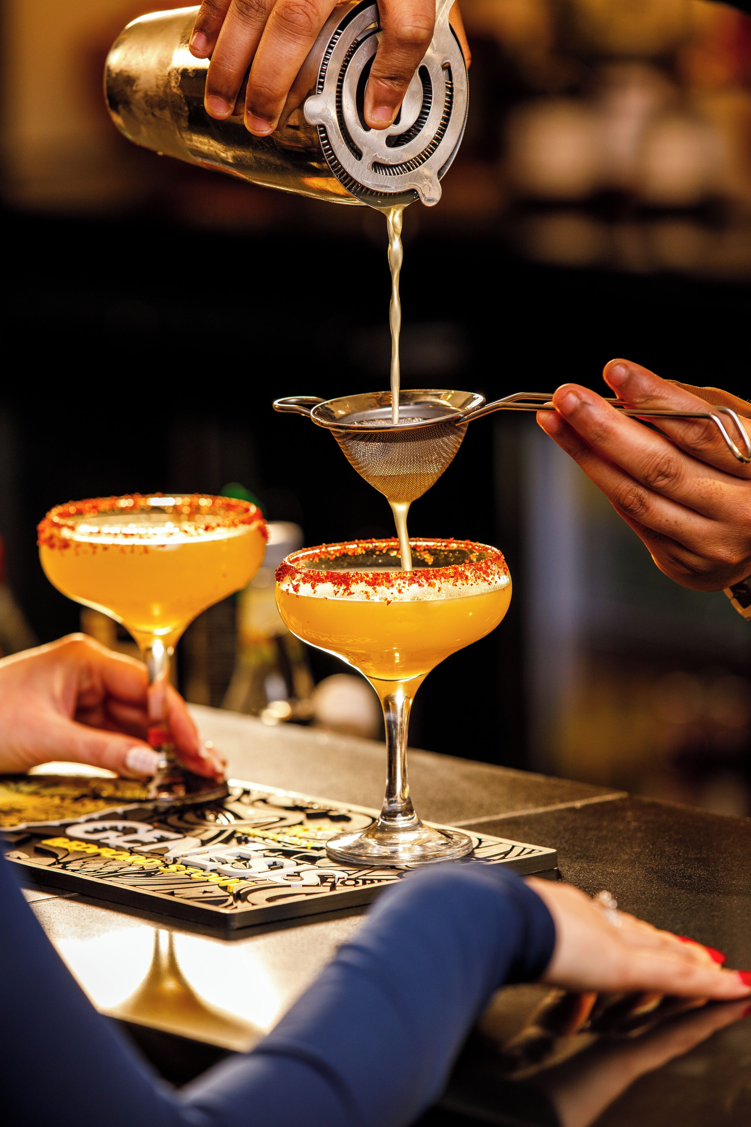 A bartender pouring a drink into a glass with a metal strainer.