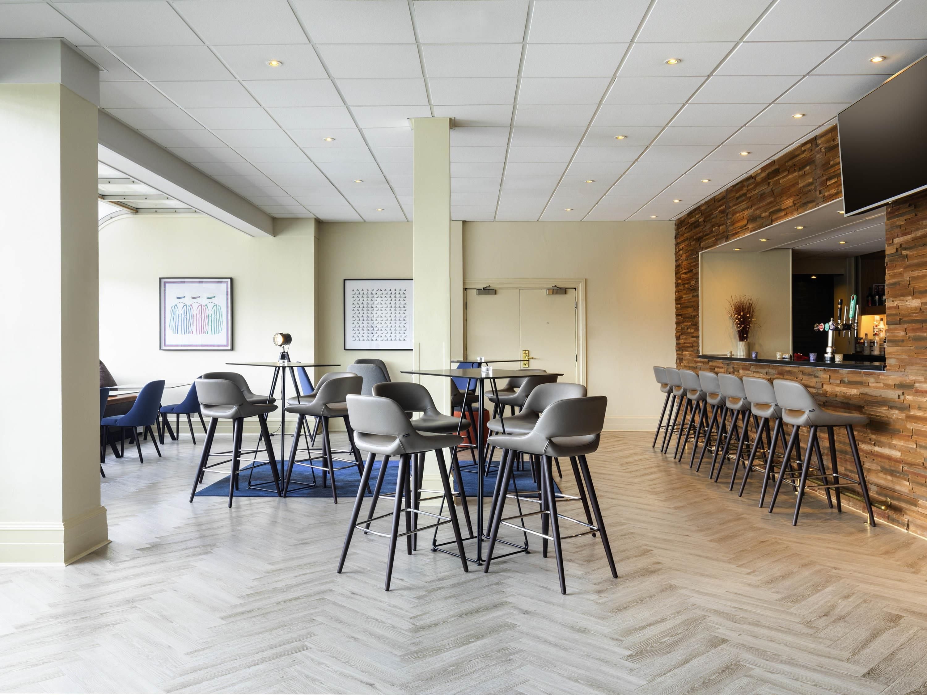 Ett modernt hotellrum med ett fiskbensmönstrat golv, en bardisk med barstolar och en stor spegel.