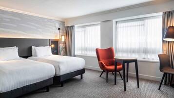 A hotel room with two beds, a small table, a chair, and a lamp.