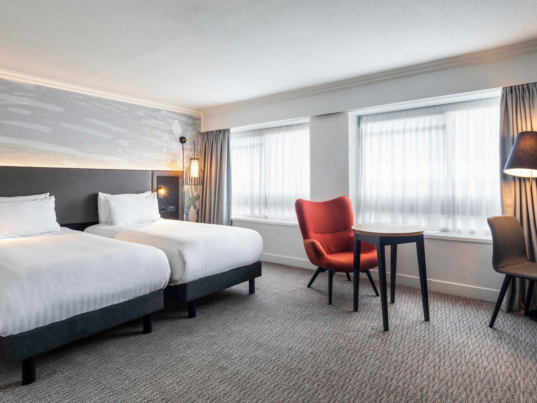 Una habitación de hotel con dos camas, una mesita, una silla y una lámpara.
