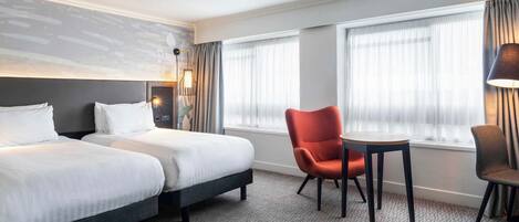 Una habitación de hotel con dos camas, una mesita, una silla y una lámpara.