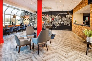 Un intérieur moderne avec un parquet en chevrons, un coin salon avec des fauteuils, un comptoir de bar et une fresque murale.