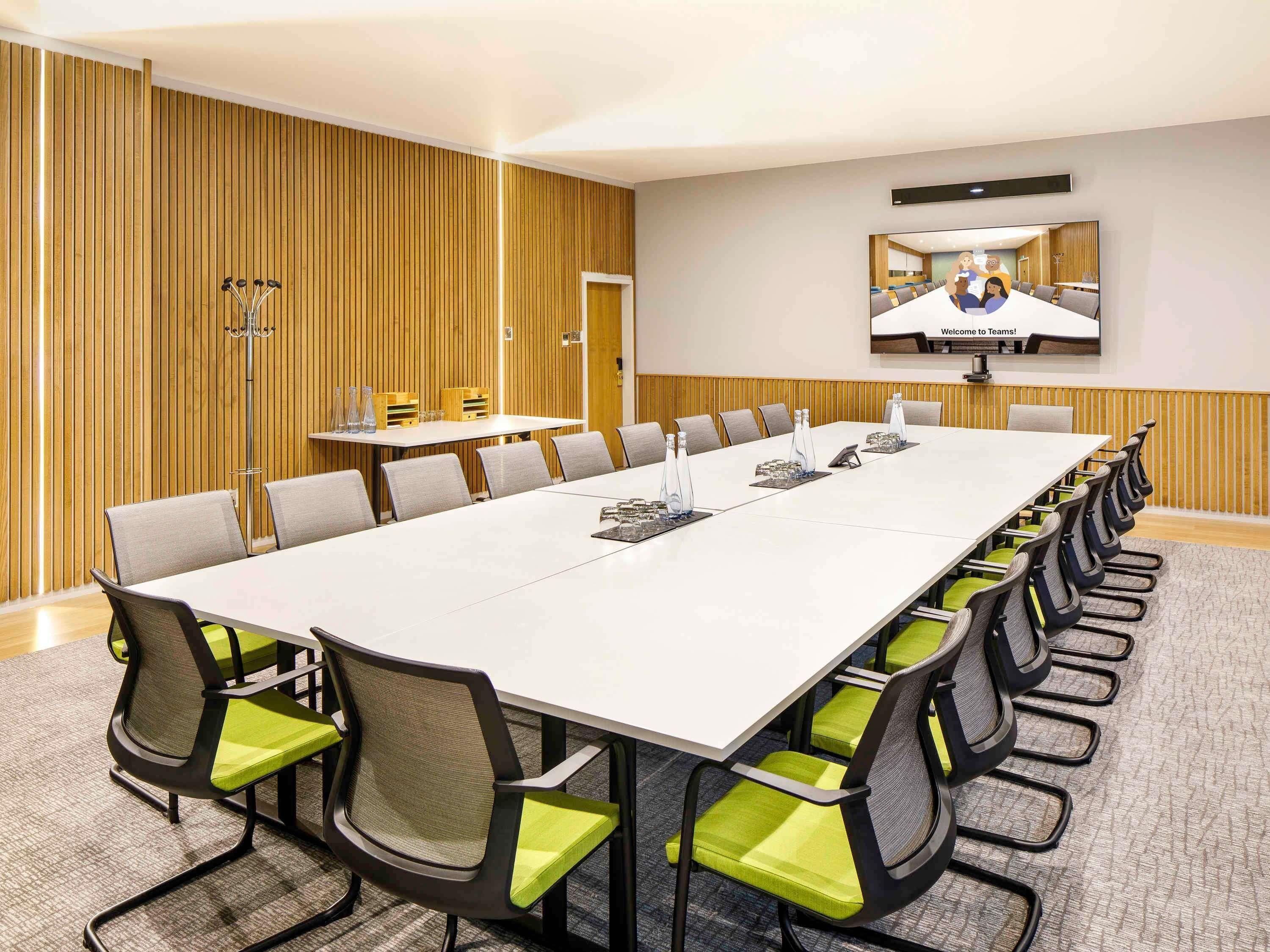 Une salle de conférence avec une longue table, des chaises, un écran de télévision et un lambris en bois.