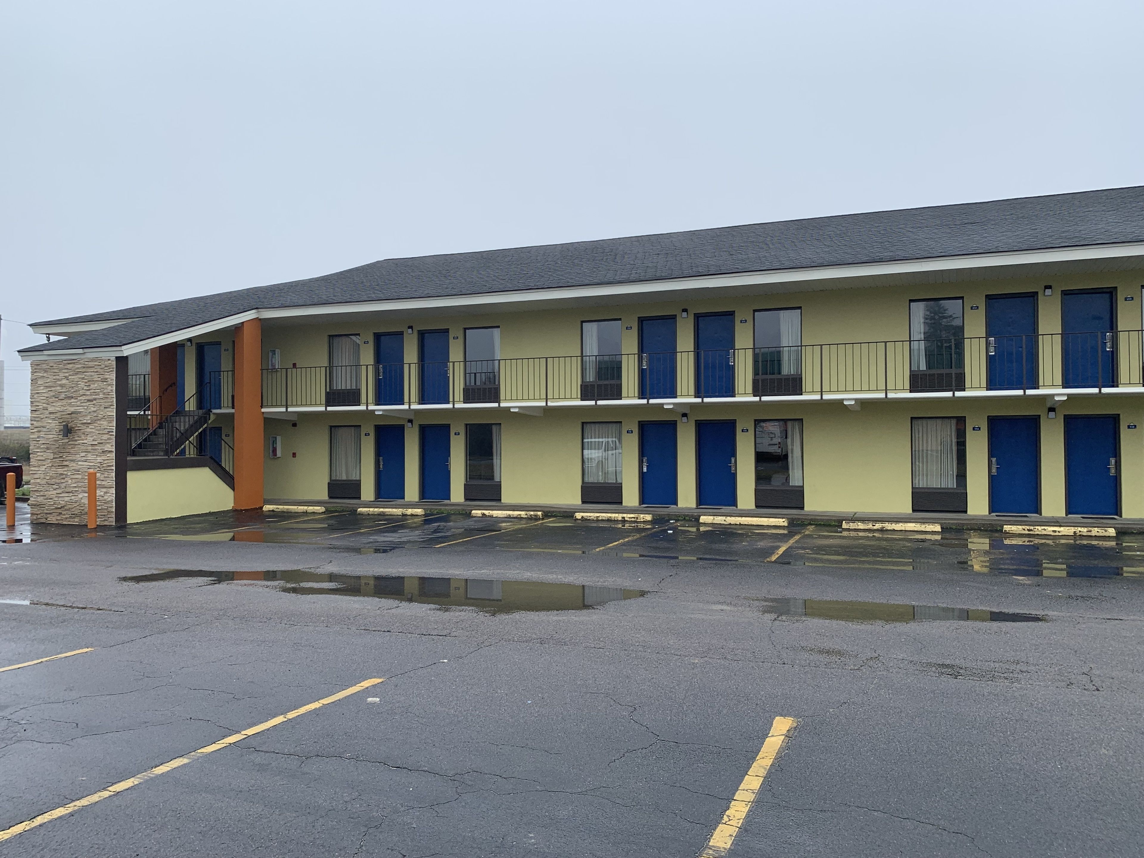 A motel with a two-story structure, multiple blue doors, and a parking lot with visible water puddles.