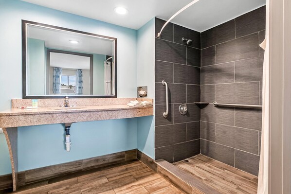 Un baño con ducha, lavamanos con espejo y un perchero para toallas.