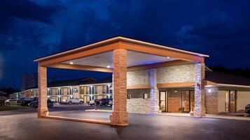 A hotel with a covered outdoor area, stone pillars, and a parking lot with several vehicles.