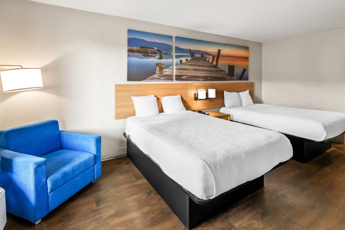 Ein Hotelzimmer mit zwei Betten, einem blauen Sessel, einem Holzkopfschild und einer Wandleuchte.
