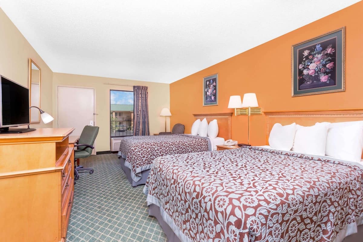 Ein Hotelzimmer mit zwei Betten, einem Schreibtisch mit Computer, einem Stuhl und einem Vorhangfenster.