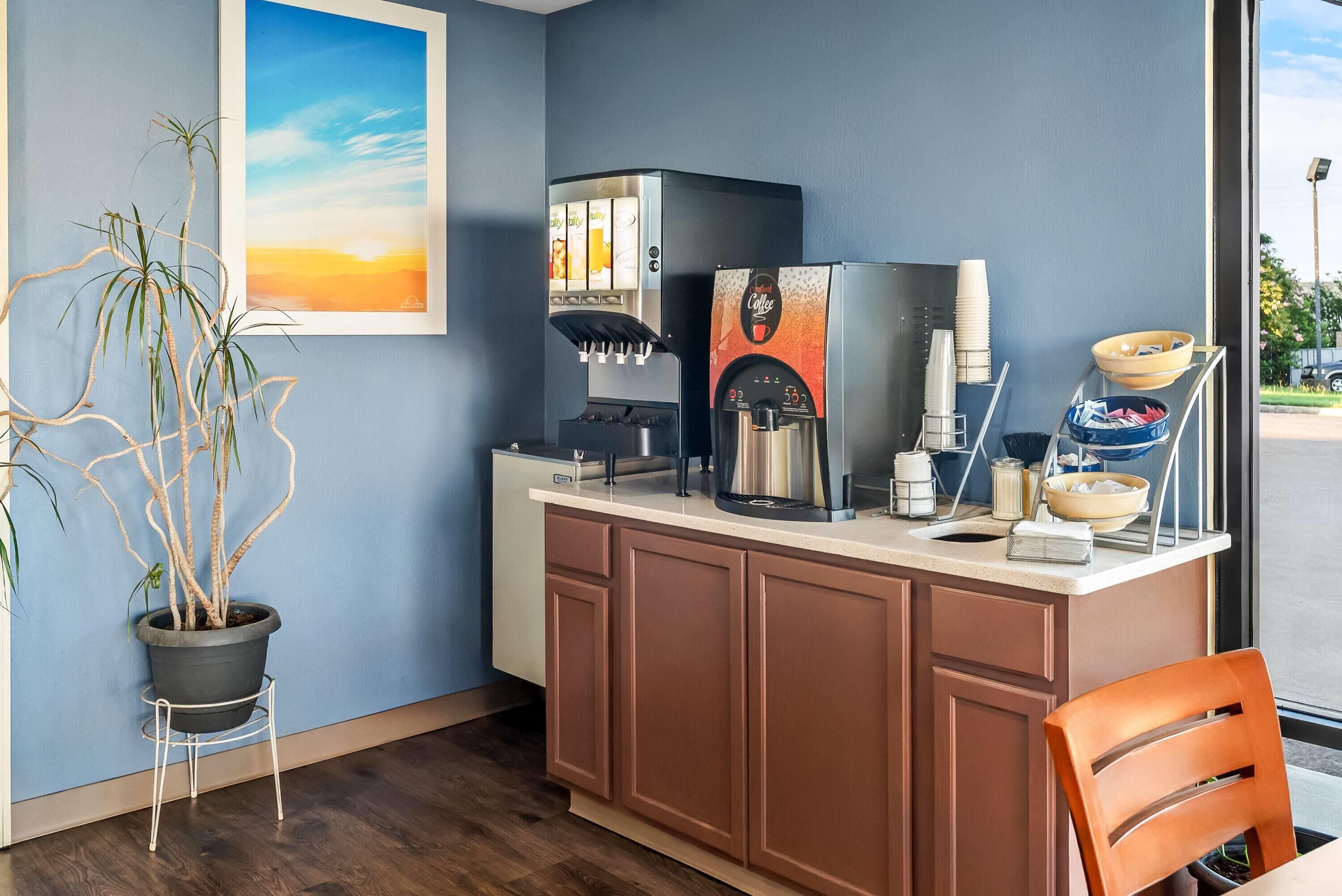 A kitchenette with a coffee machine, a potted plant, and a framed picture on the wall.