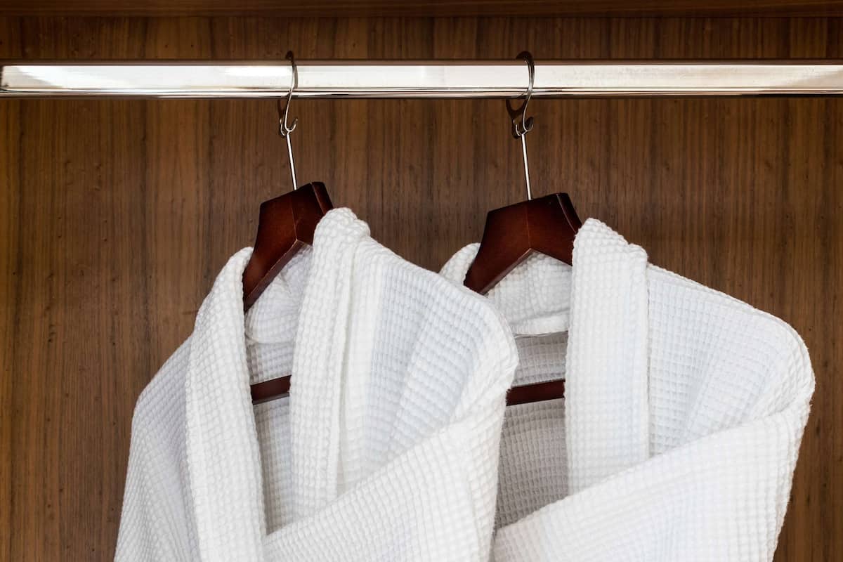 Two white bathrobes hanging on a wooden rack.
