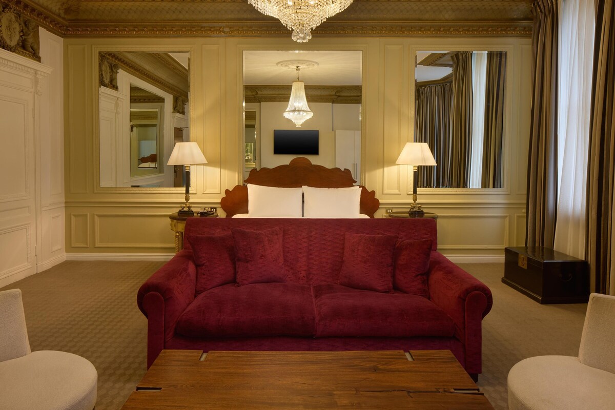 A hotel room with a large bed, two bedside lamps, a wooden coffee table, and a red sofa.