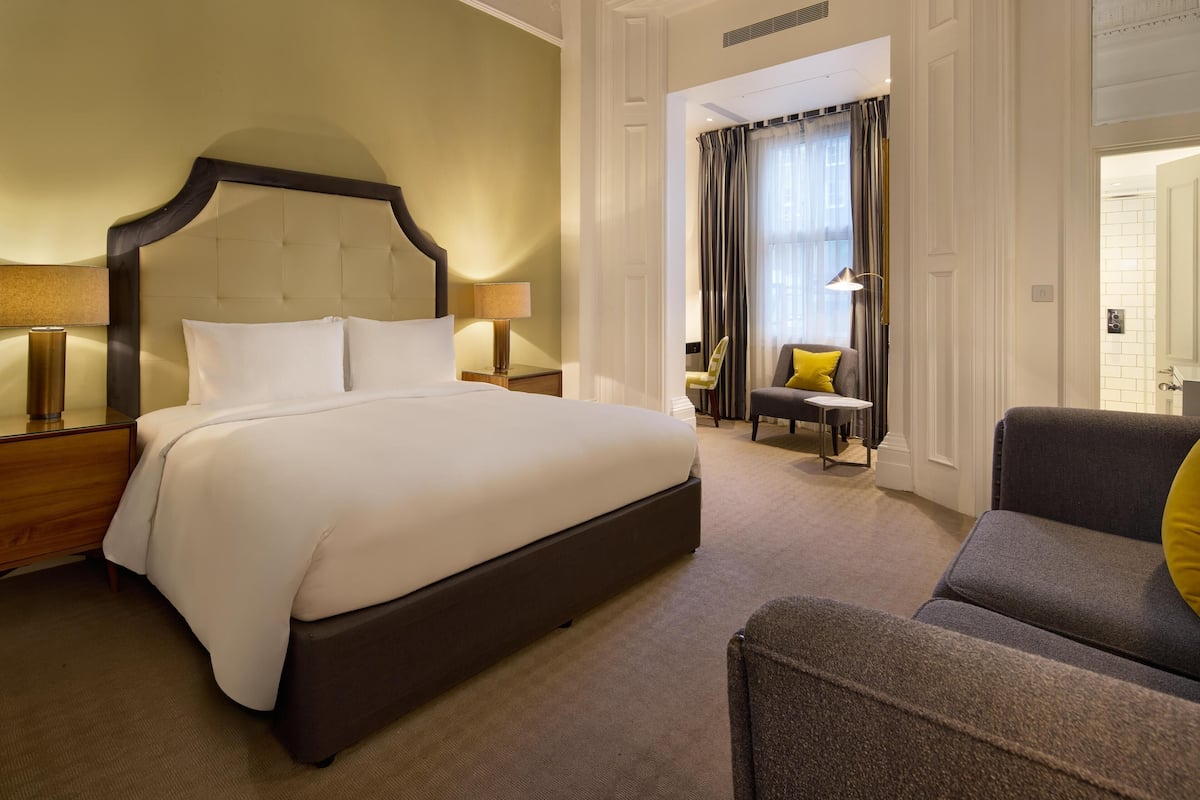 A hotel room with a large bed, a sitting area with a sofa and armchair, and a small table.