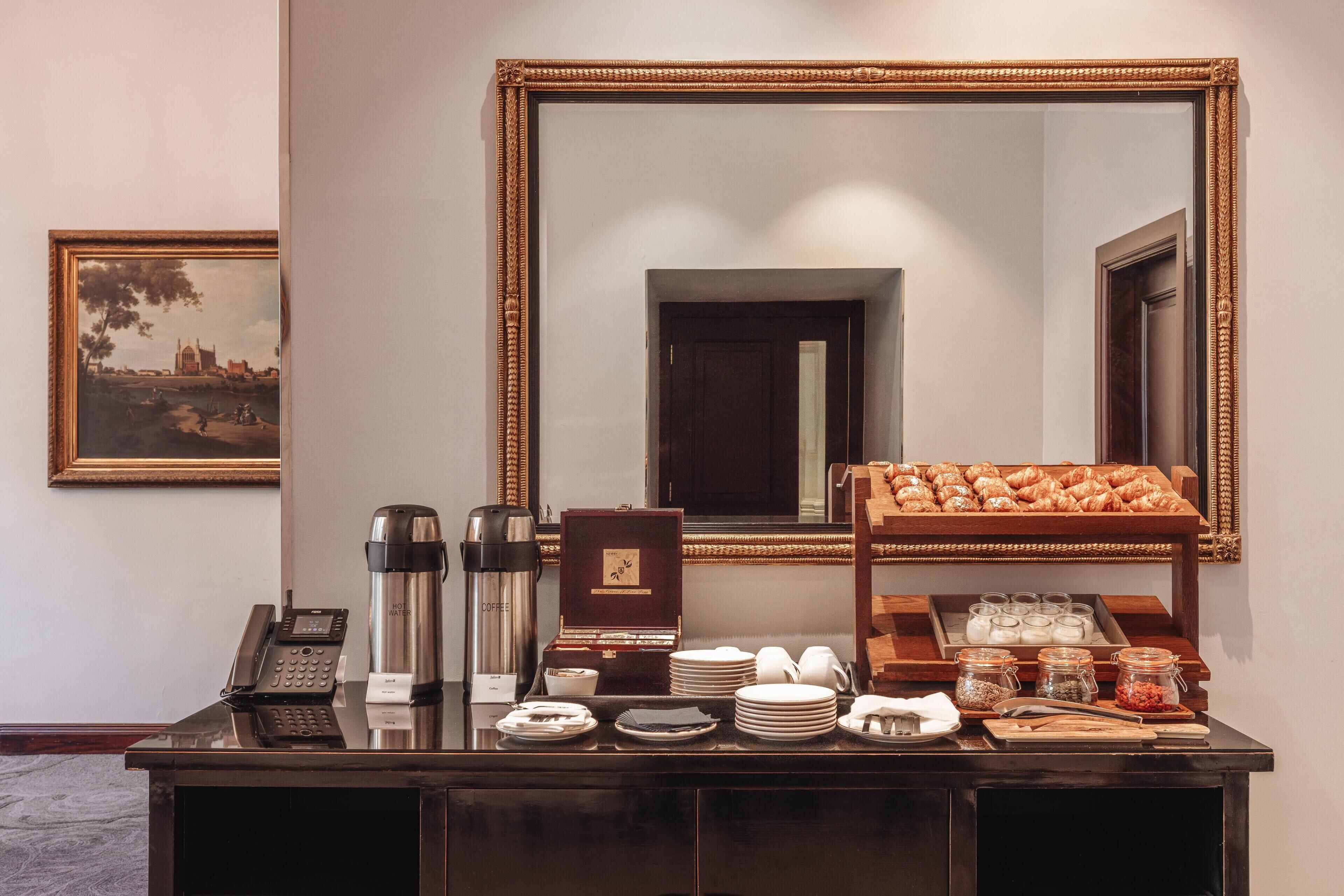 A hotel reception area with a coffee station, a telephone, and a framed painting on the wall.