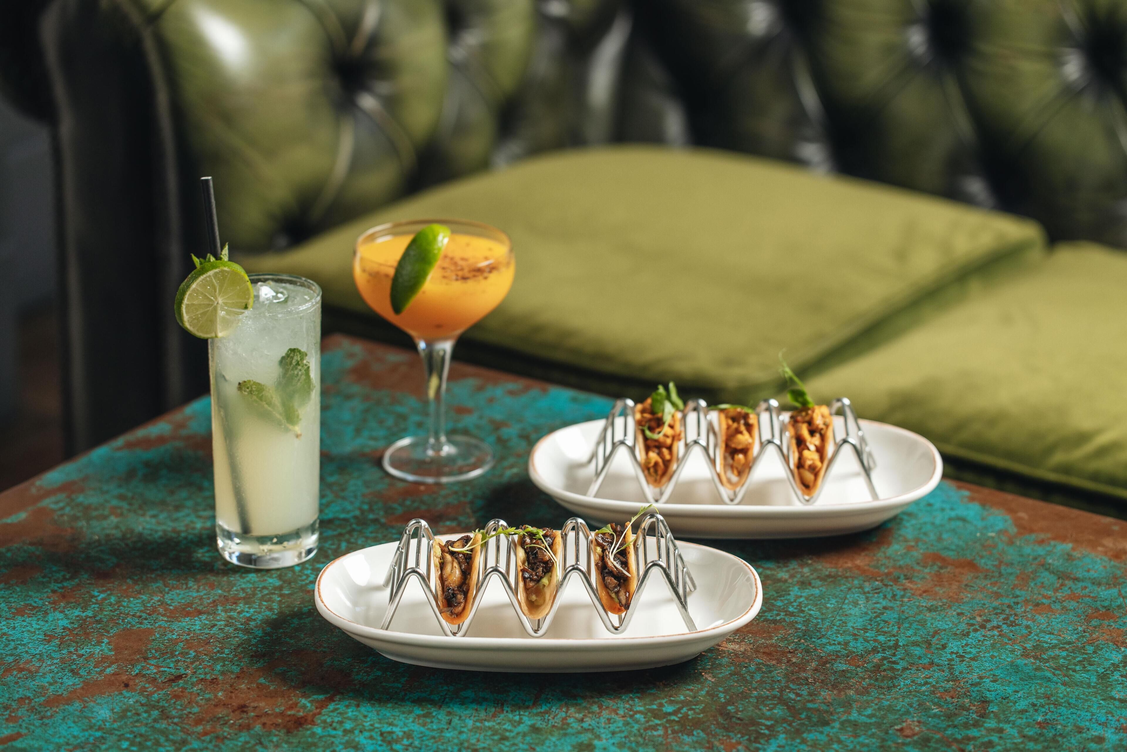 A table with a drink, a plate of food, and a green cushioned chair in the background.
