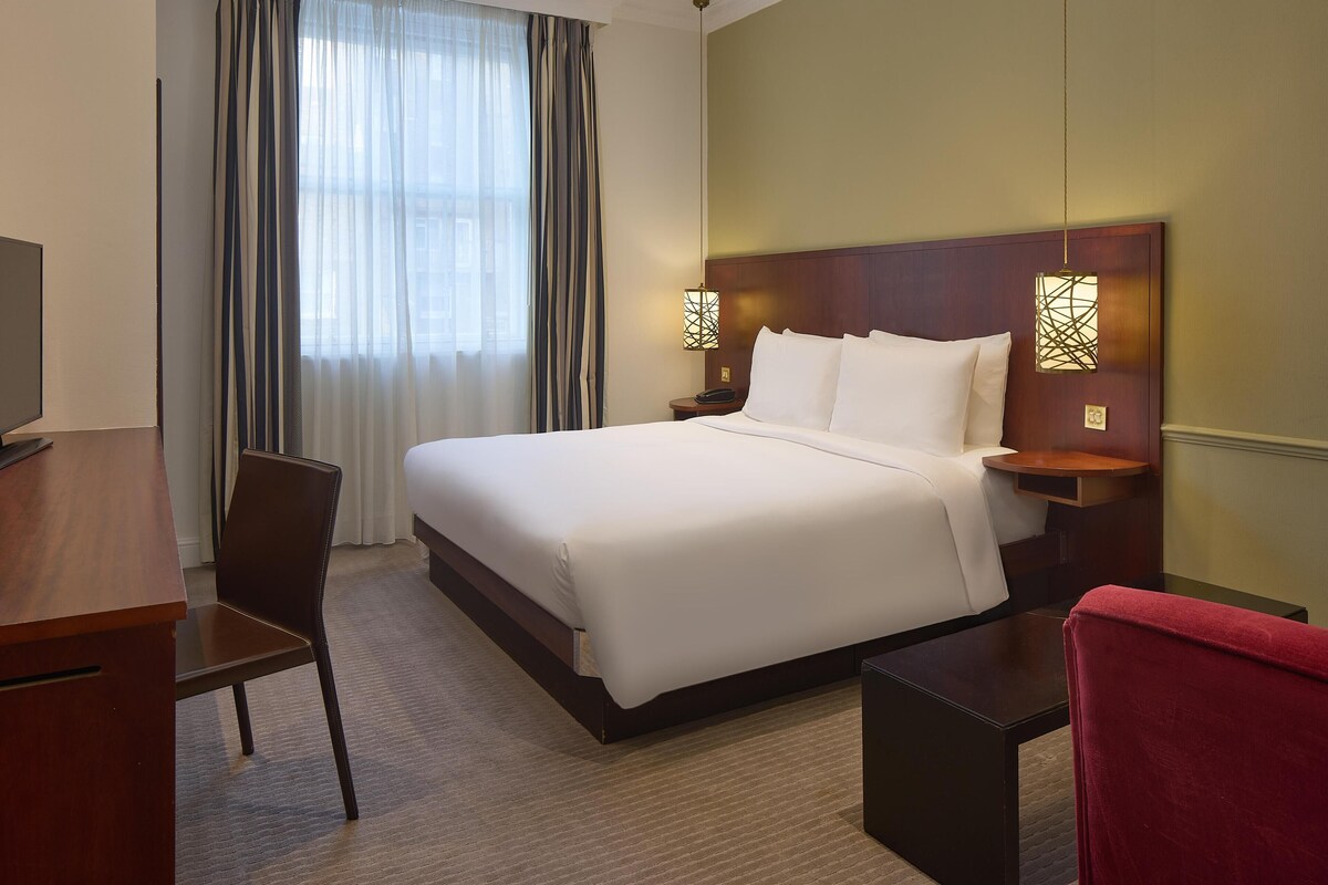 A hotel room with a large bed, a desk, a chair, and a TV.