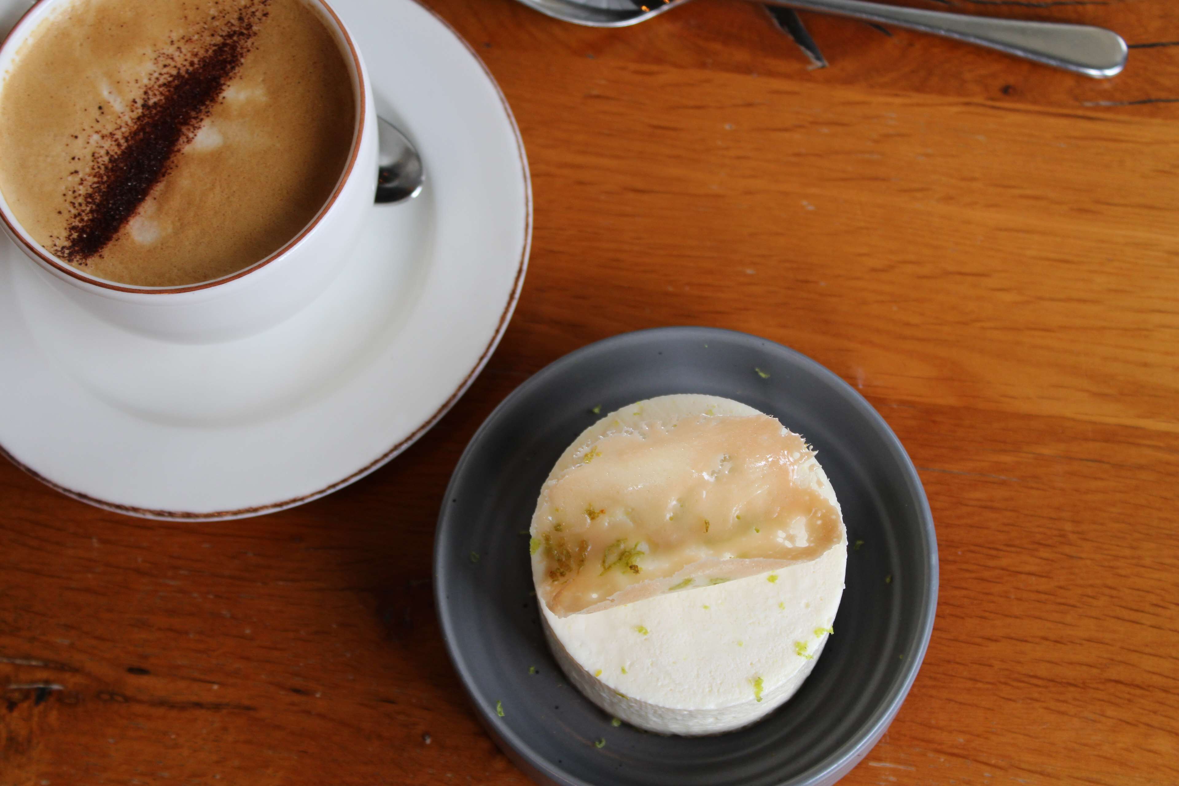 A cup of coffee and a dessert on a wooden table.
