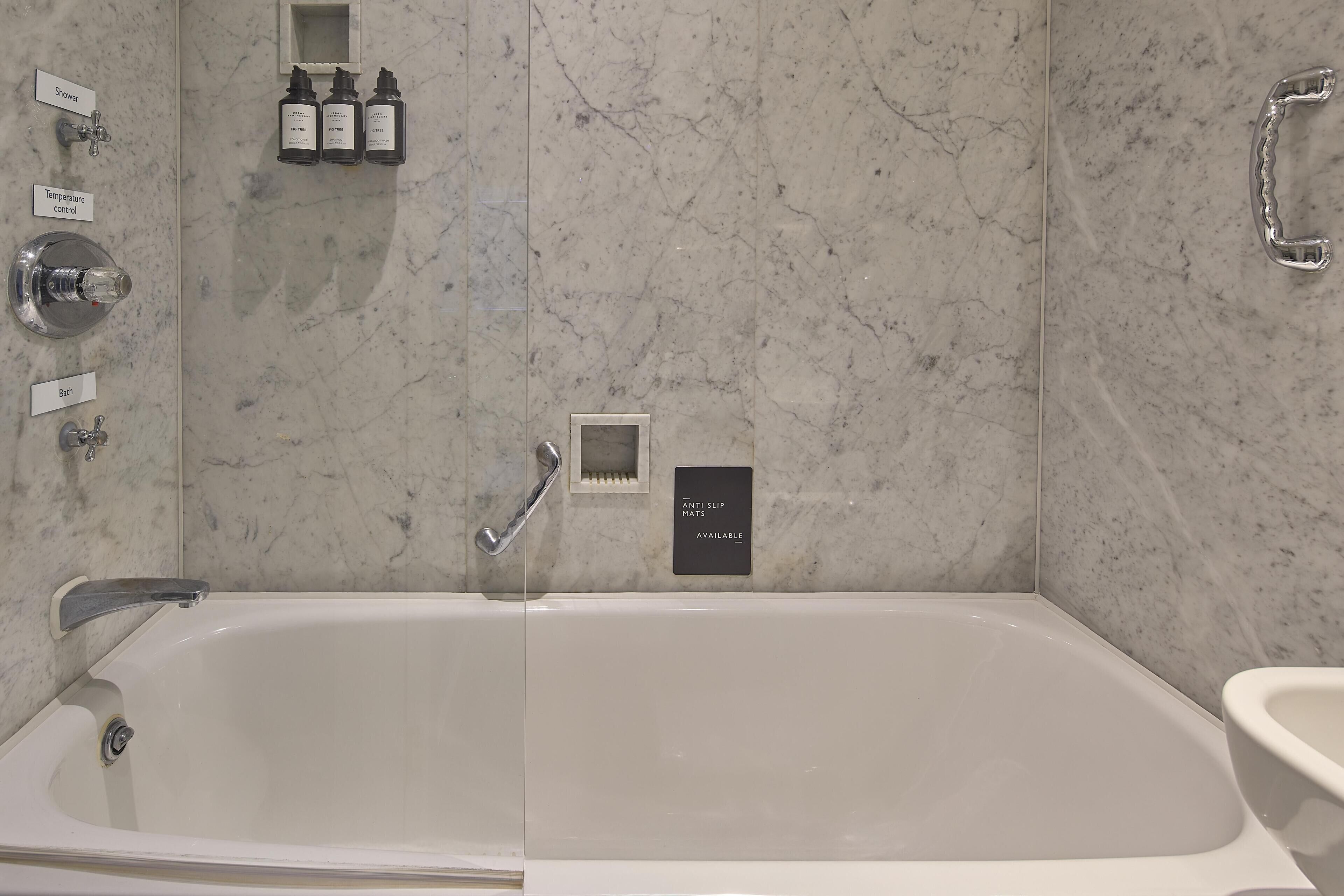 Un baño moderno con una bañera grande, ducha y control de temperatura. También hay botellas de champú y acondicionador en la pared.