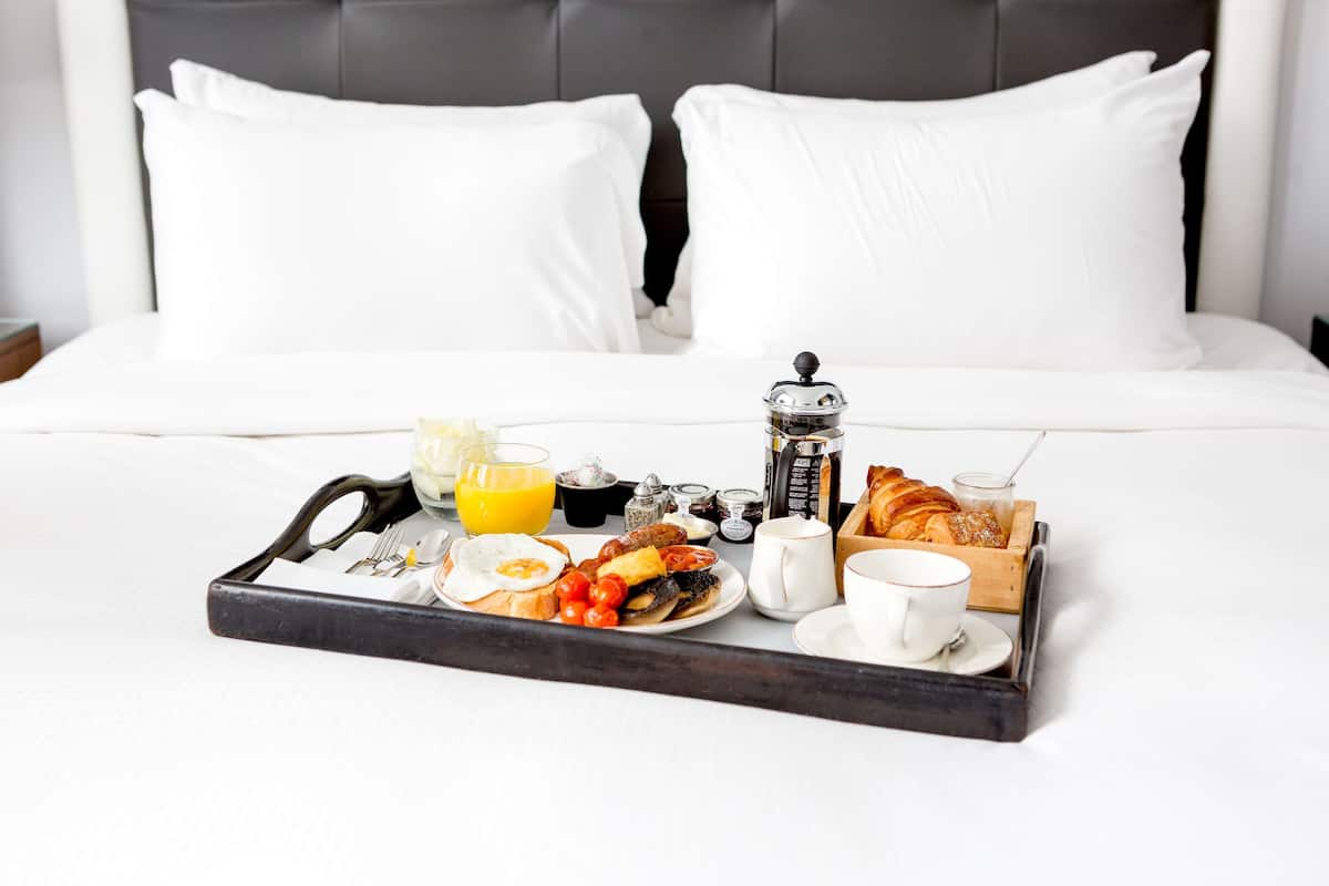 A breakfast tray on a bed with white bedding and a dark headboard.