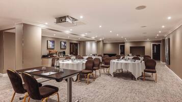 A conference room with round tables, chairs, a projector, and a kitchenette area.
