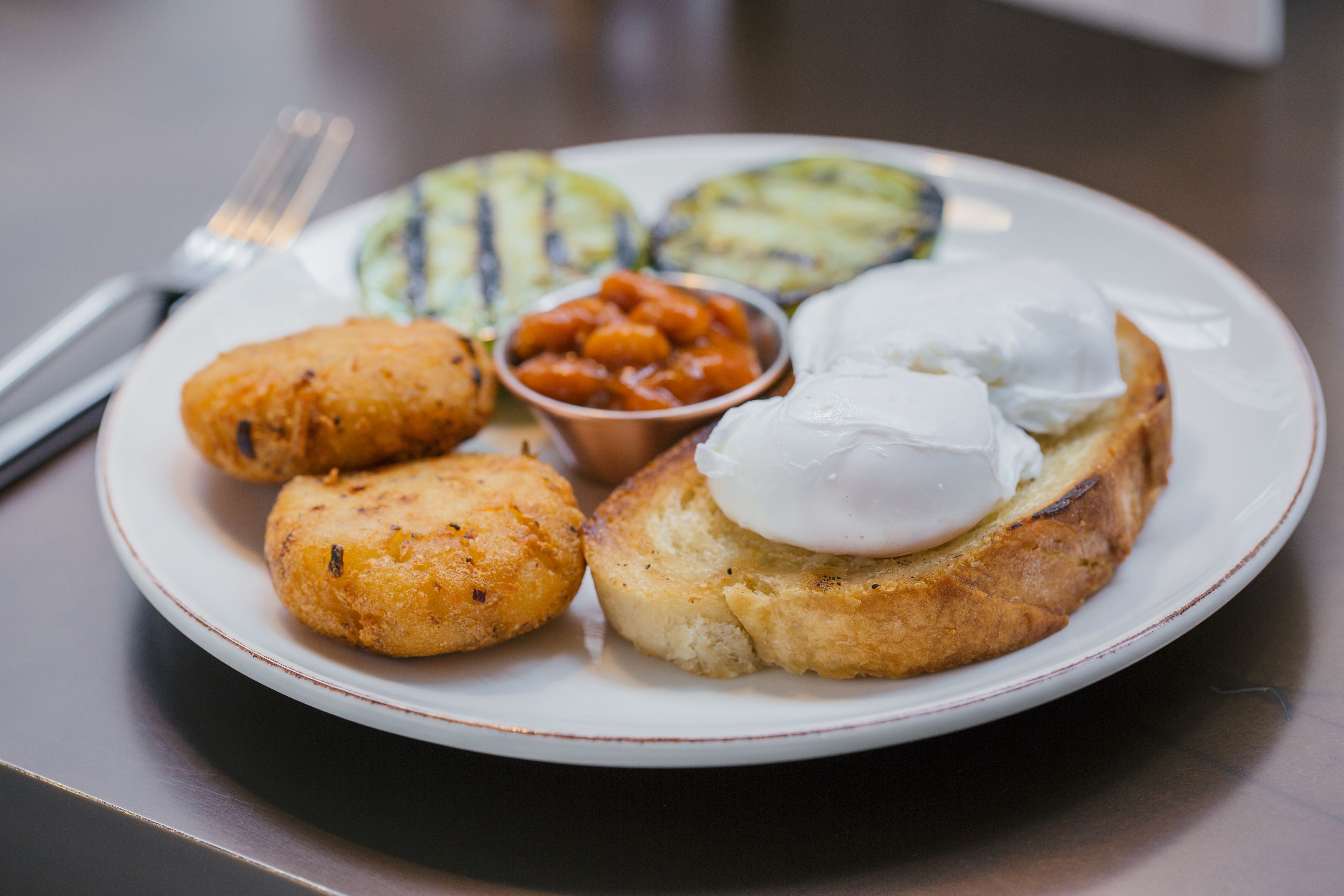 A plate with food items including a poached egg, fried items, and a small bowl of sauce.