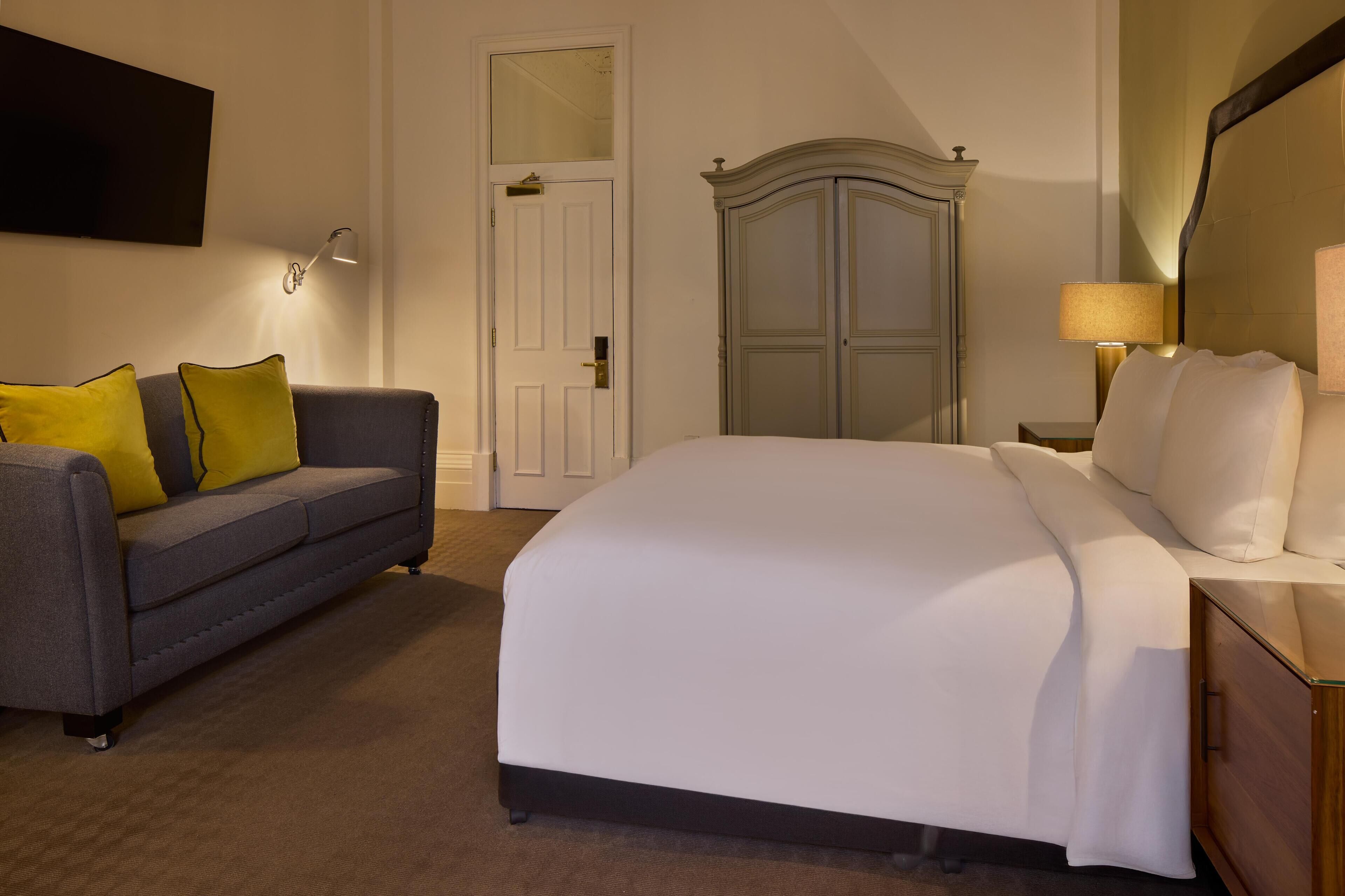 A hotel room with a bed, a sofa, a wardrobe, and a mirror.